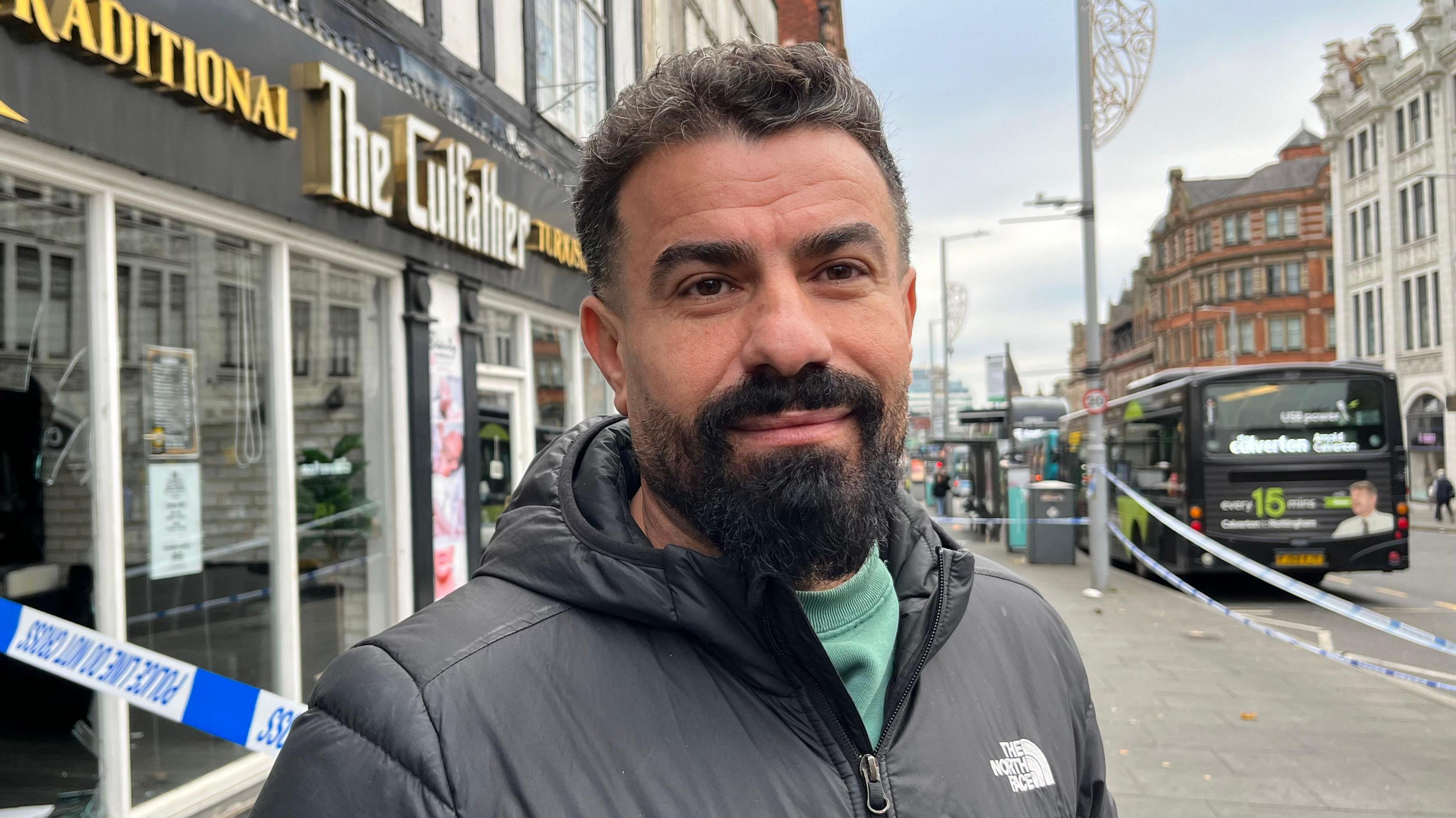 Barber shop owner Kadir Bulanur standing in front of The Cutfather barbershop wearing a black jacket