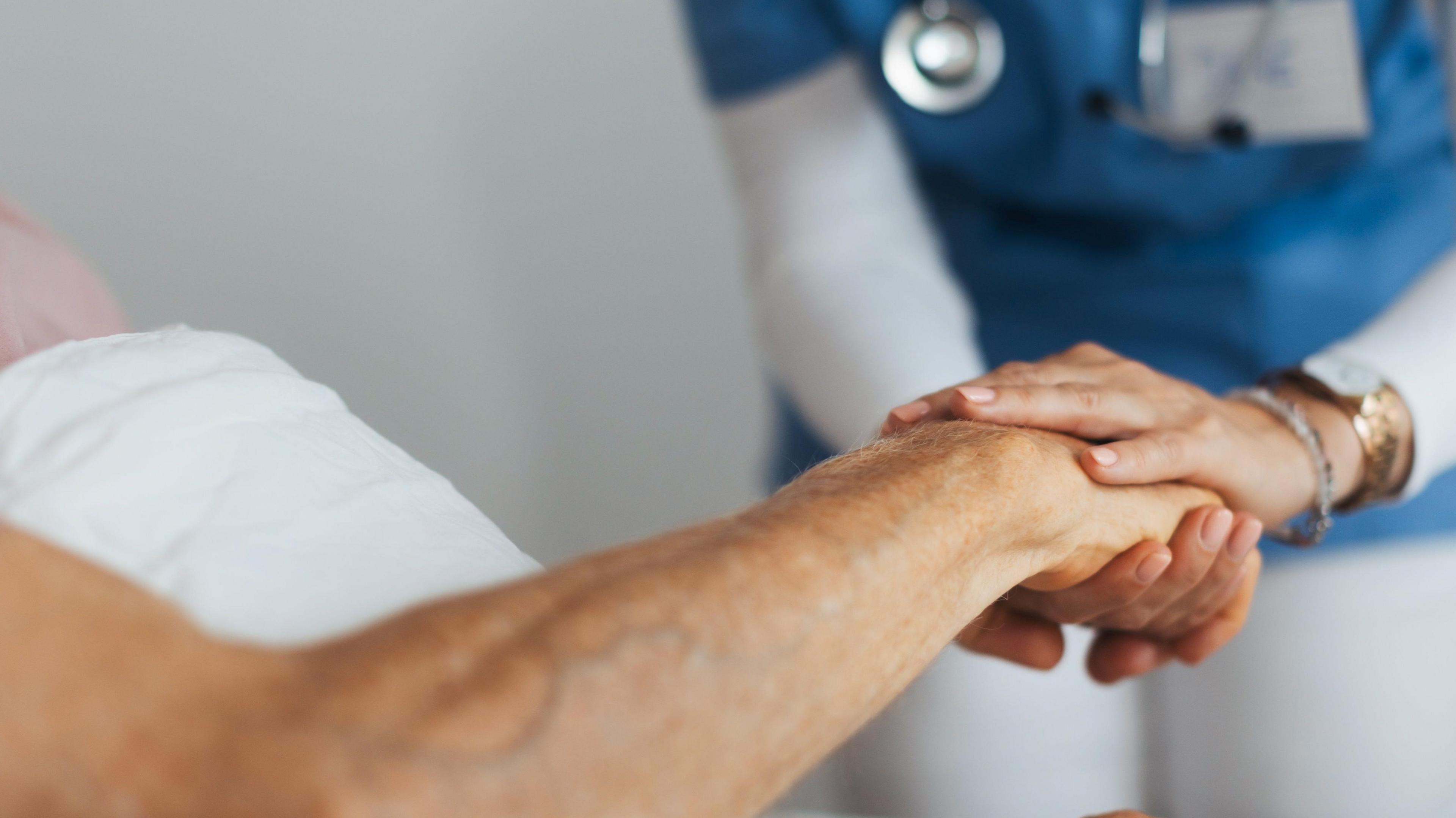 Stock image shows the arm of an unidentified patient extending from a bed and held in the hands of a nurse