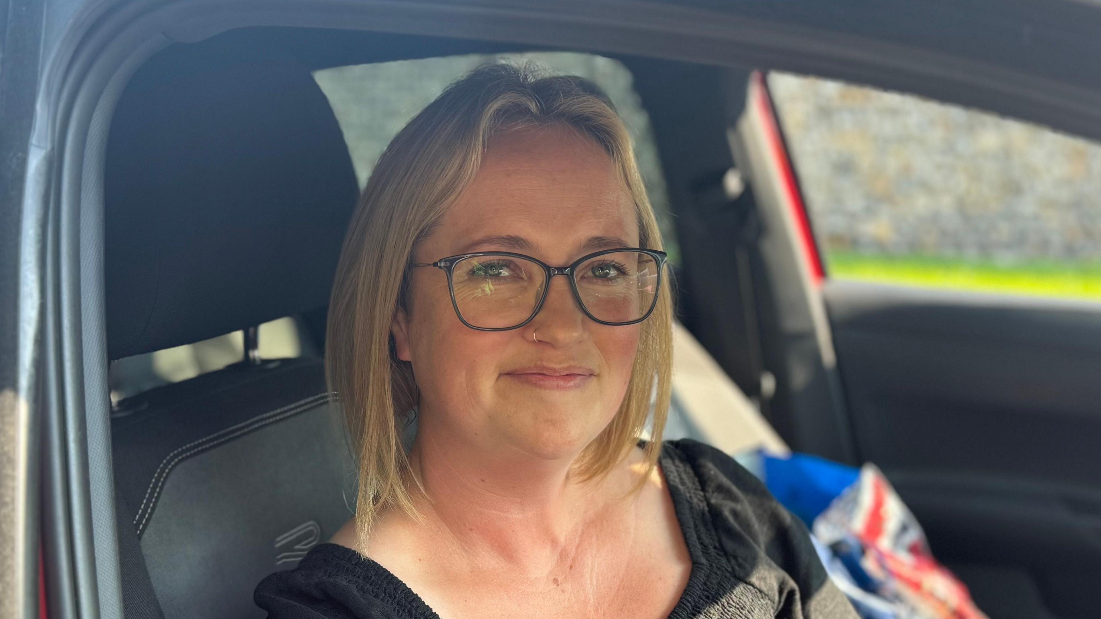 A woman with blonde hair and glasses smiling into the camera