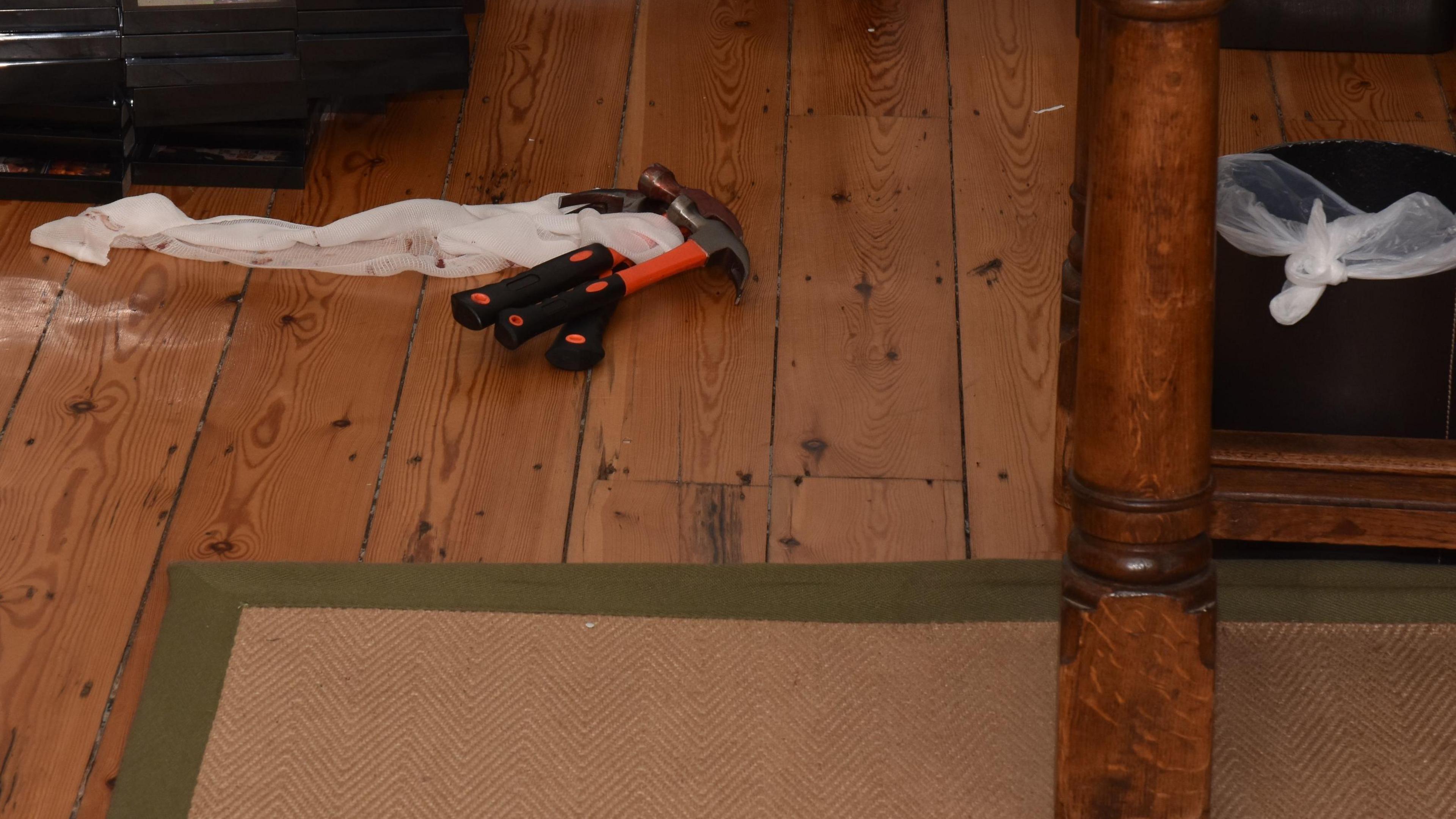 Image shows weapons on the a wooden floor. The claw hammers have orange and black handers. 