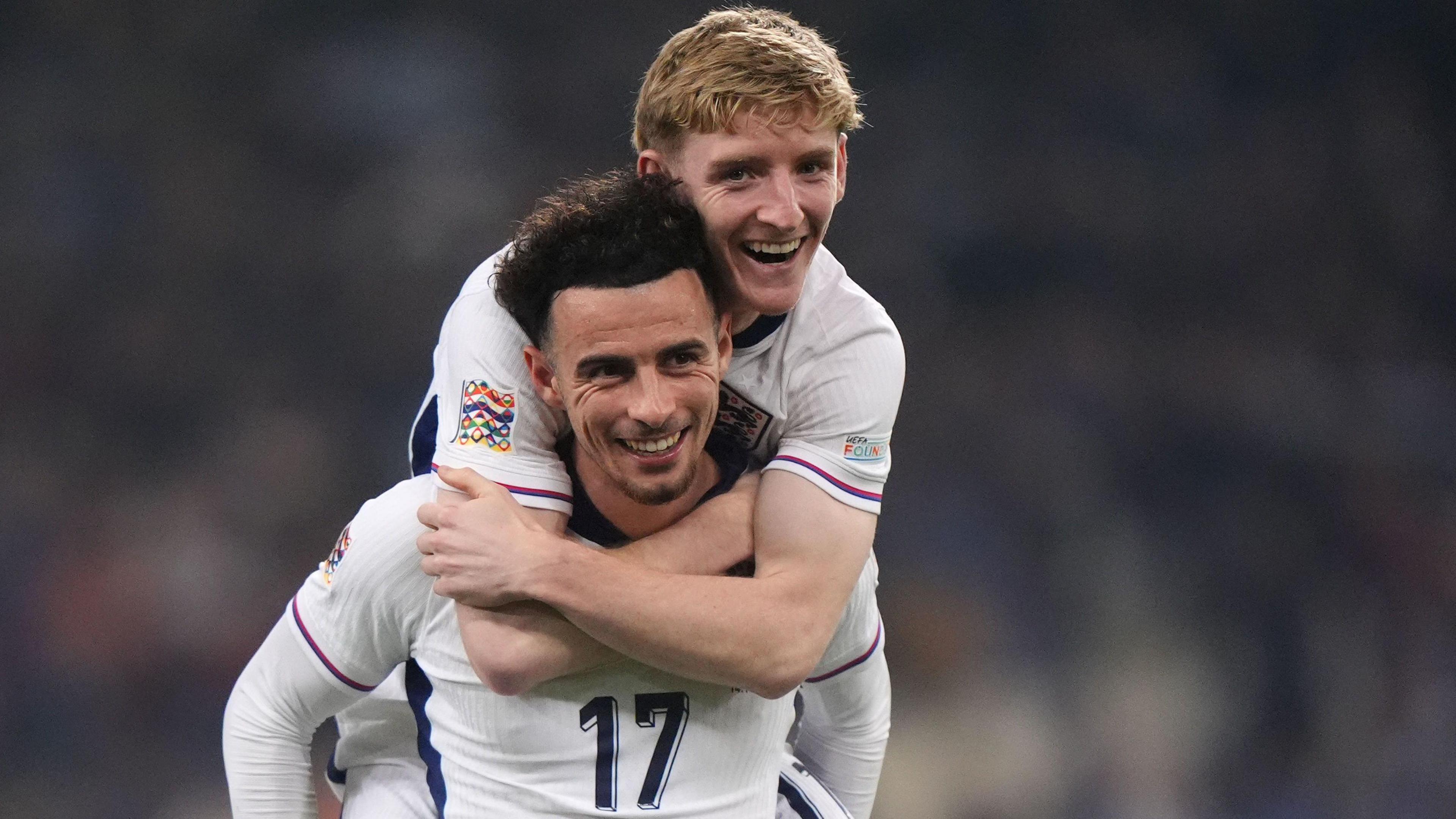 Curtis Jones and Anthony Gordon celebrate England's win. Gordon jumps on Jones' back and wraps his arms around him. 