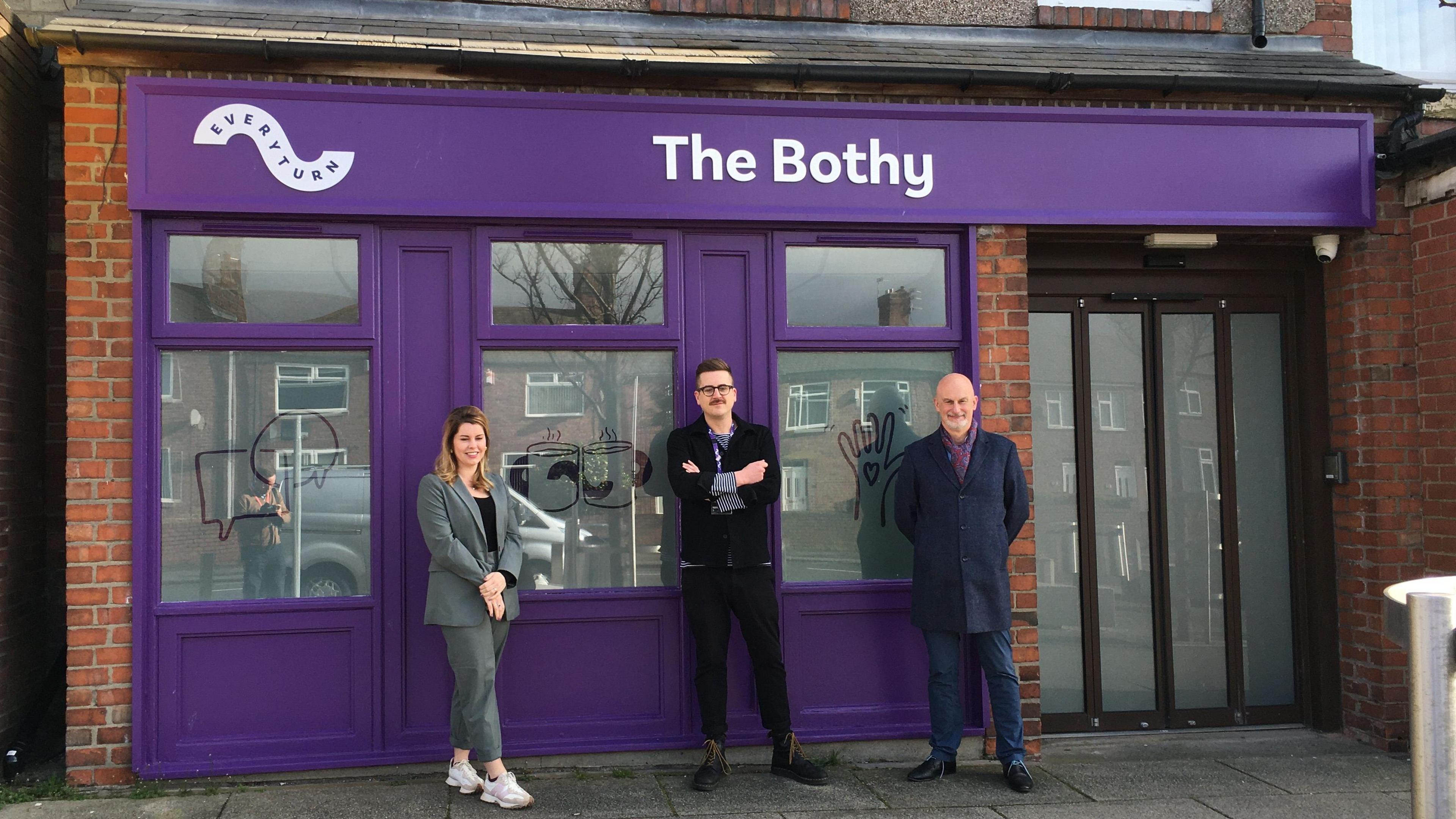 Three people standing outside purple shop front of The Bothy in Ashington