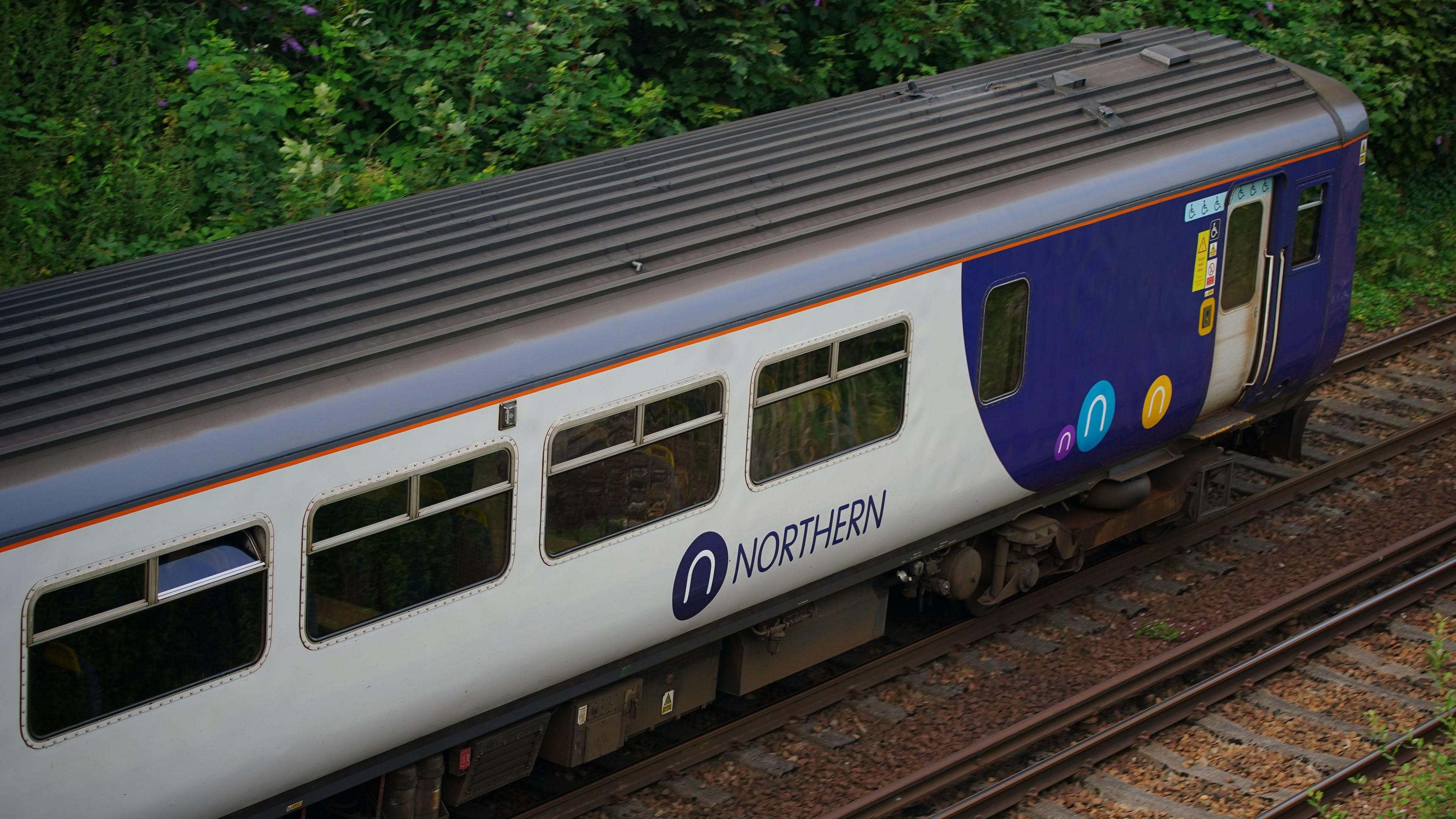 A grey and purple Northern train on a track with green bushes in the background.