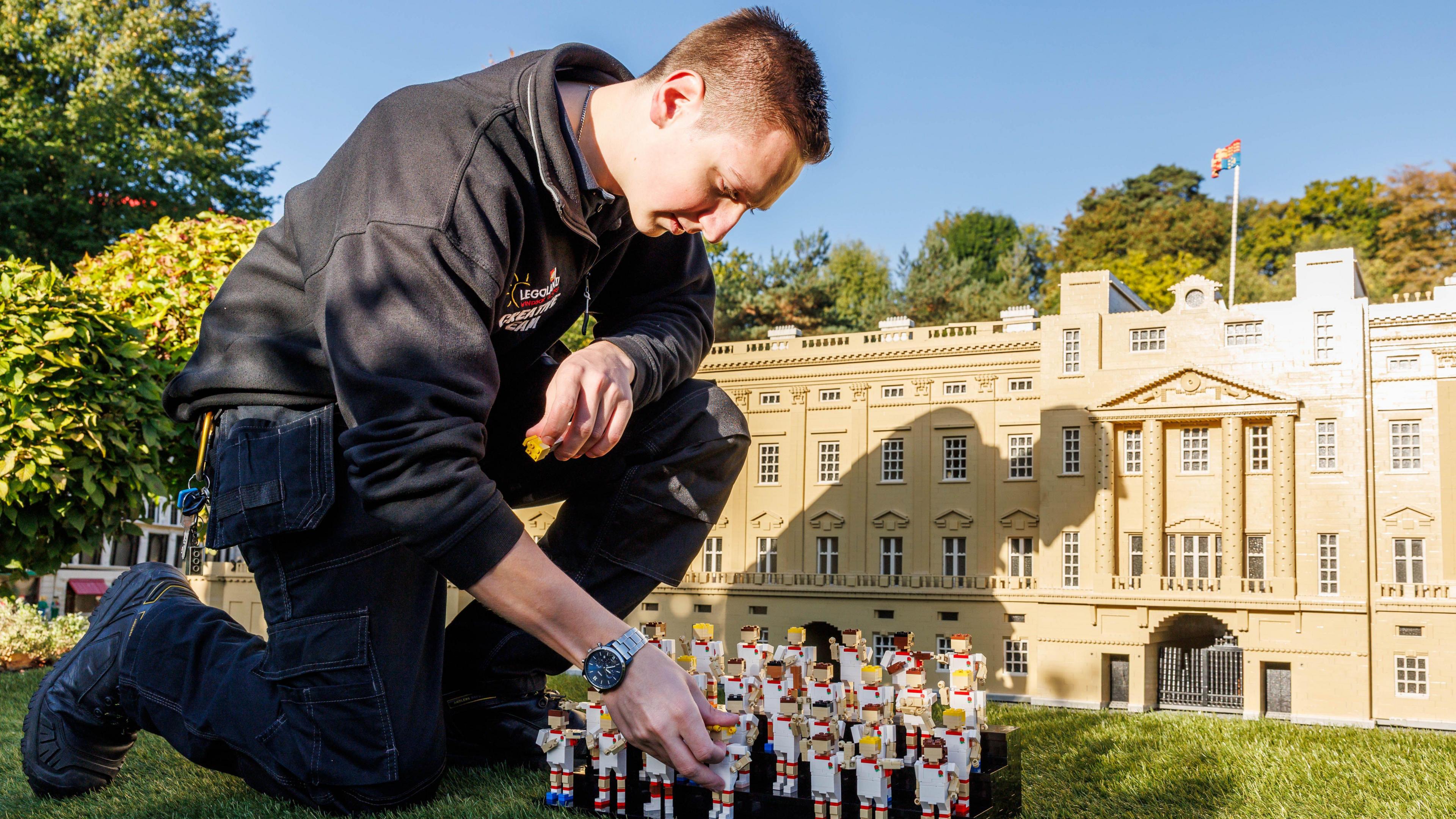 Daniel Brown is crouched down fiddling with the Red Roses Lego display,