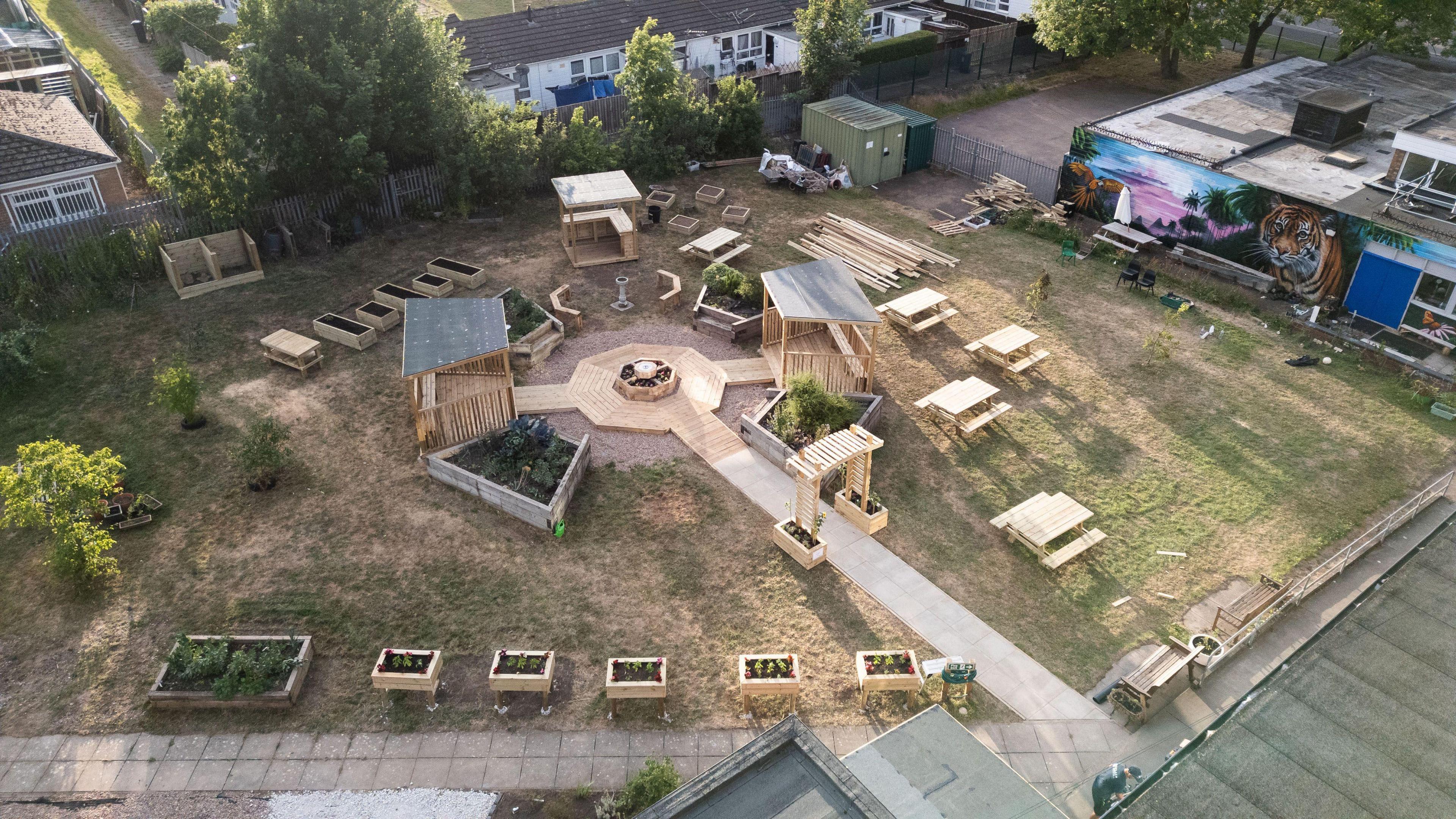 A drone shot of the finished garden from above. It shows wooden planters and benches on a grass space.