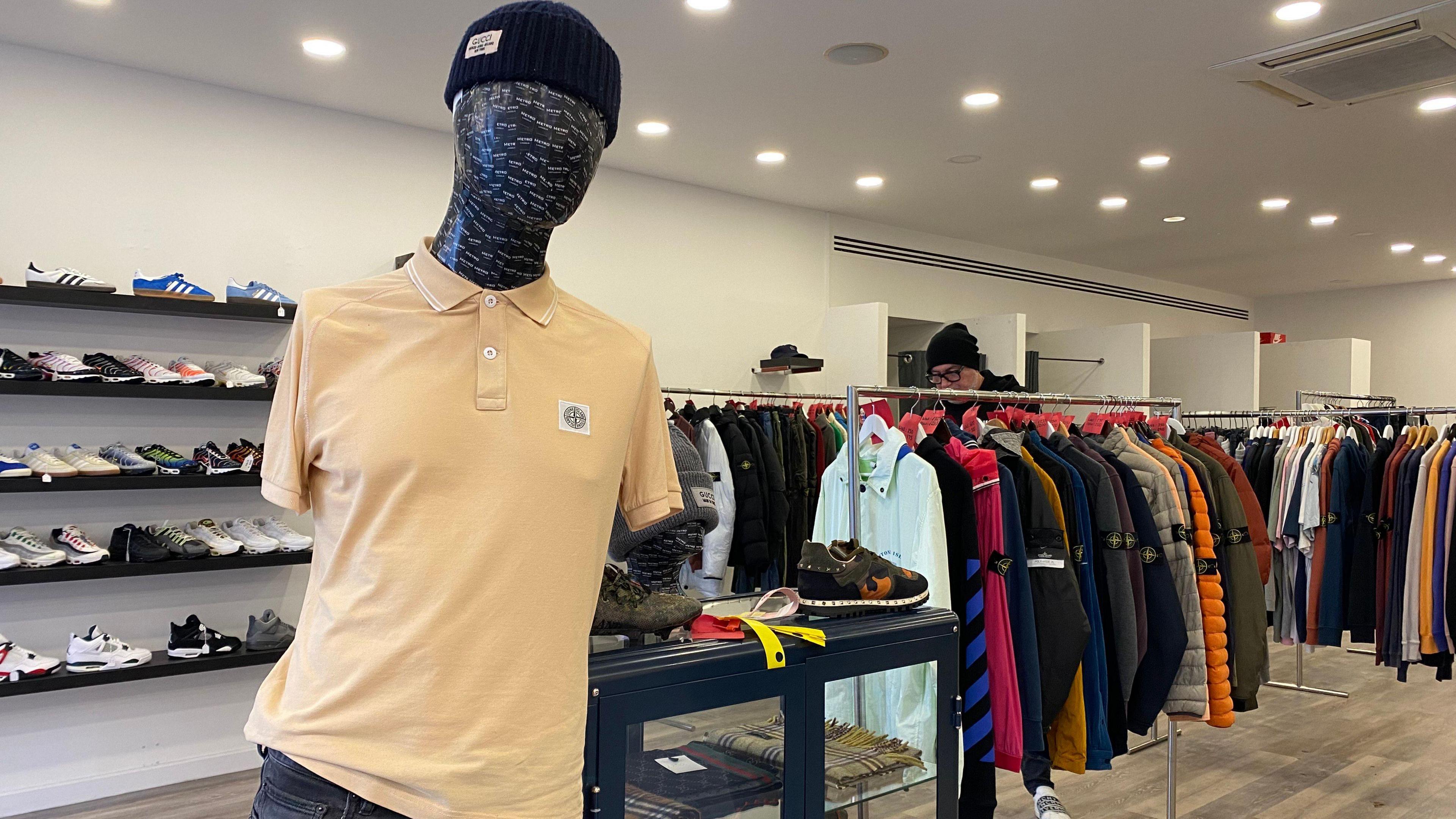 A mannequin inside of a shop with clothing rails and trainers displayed in the background