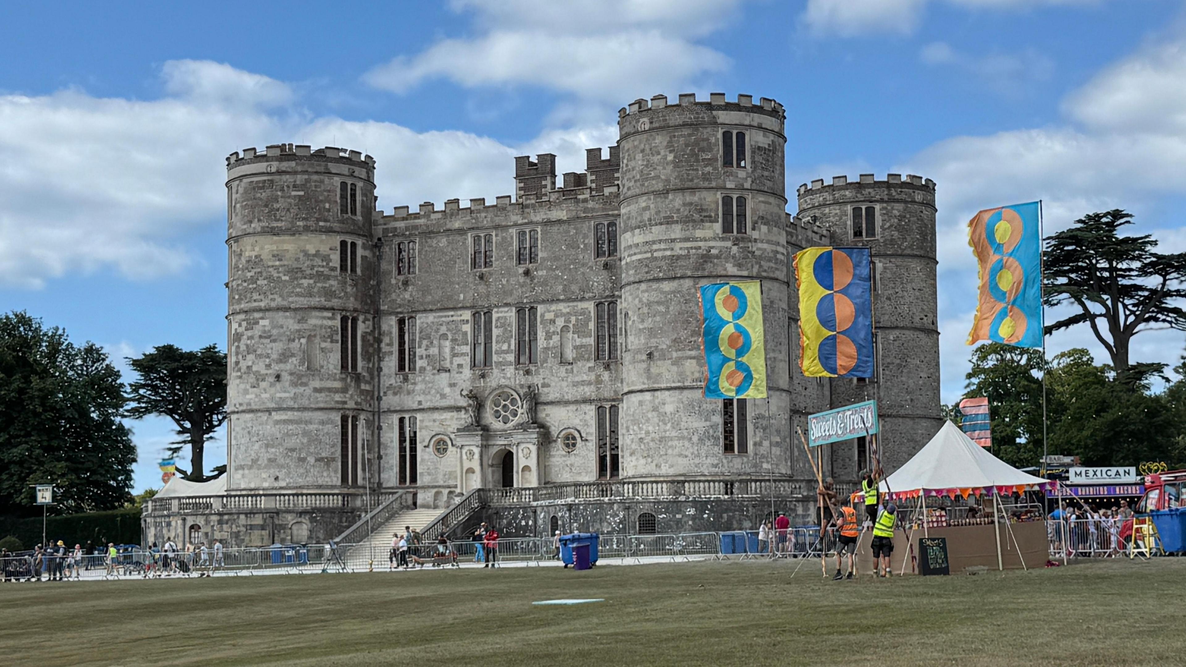 Lulworth Castle is a traditional castle surrounded by grass fields, with festival flags and banners around it.