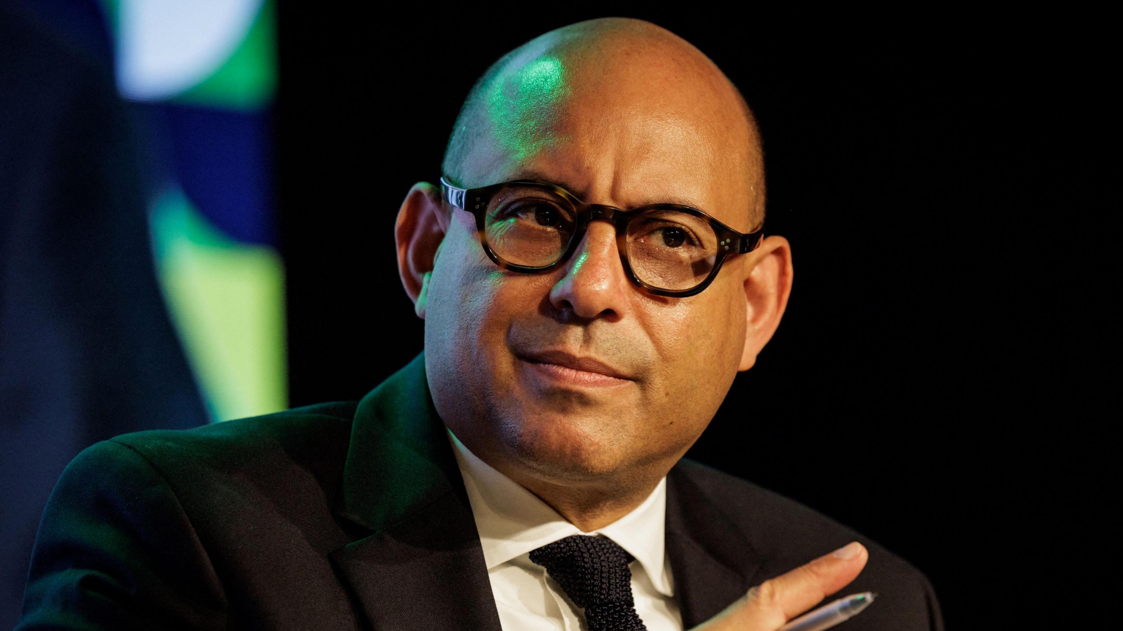 Simon Stiell wears a black suit, white shirt and black tie. 