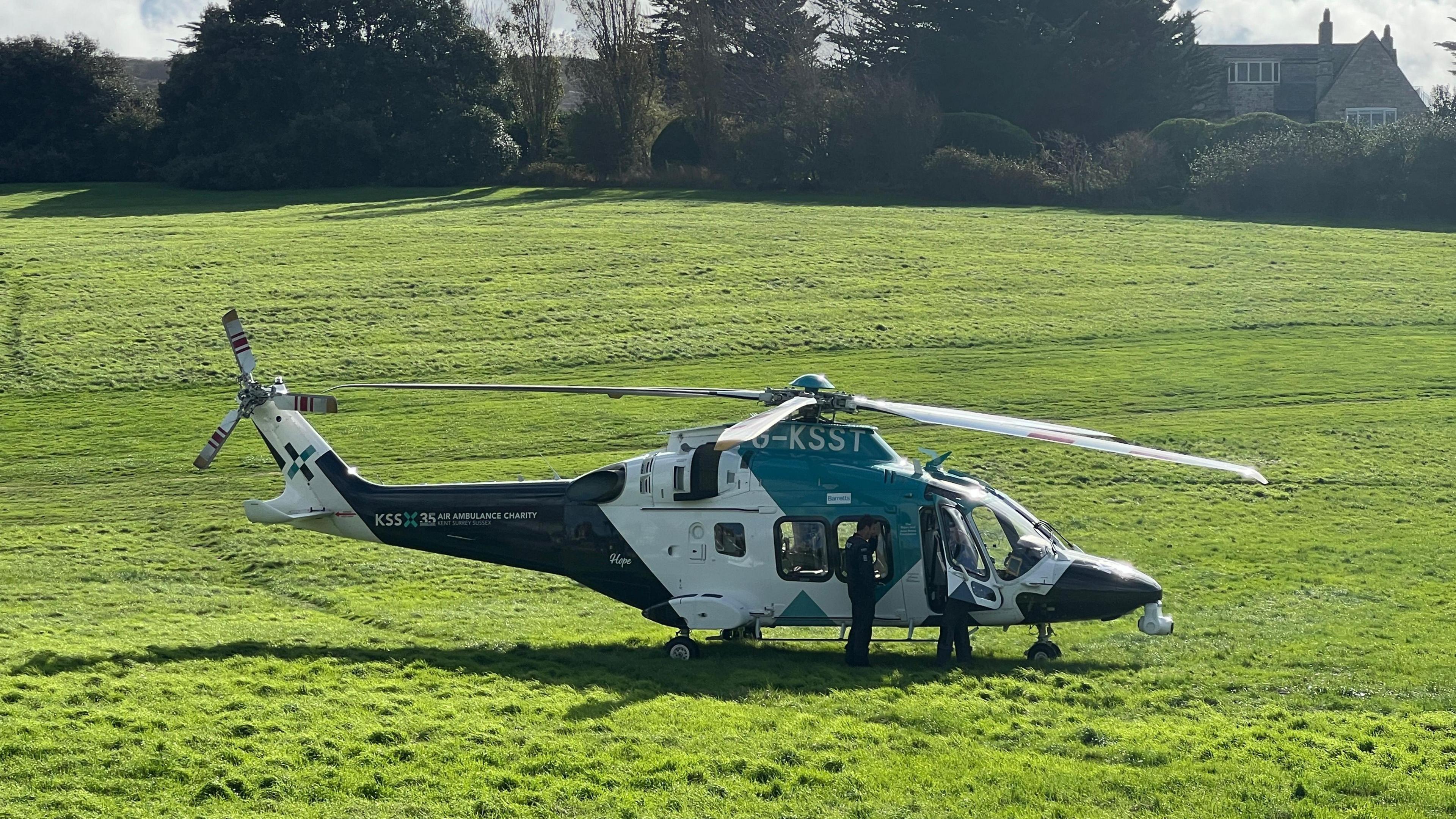 A helicopter on a field. There are two emergency workers standing by it.