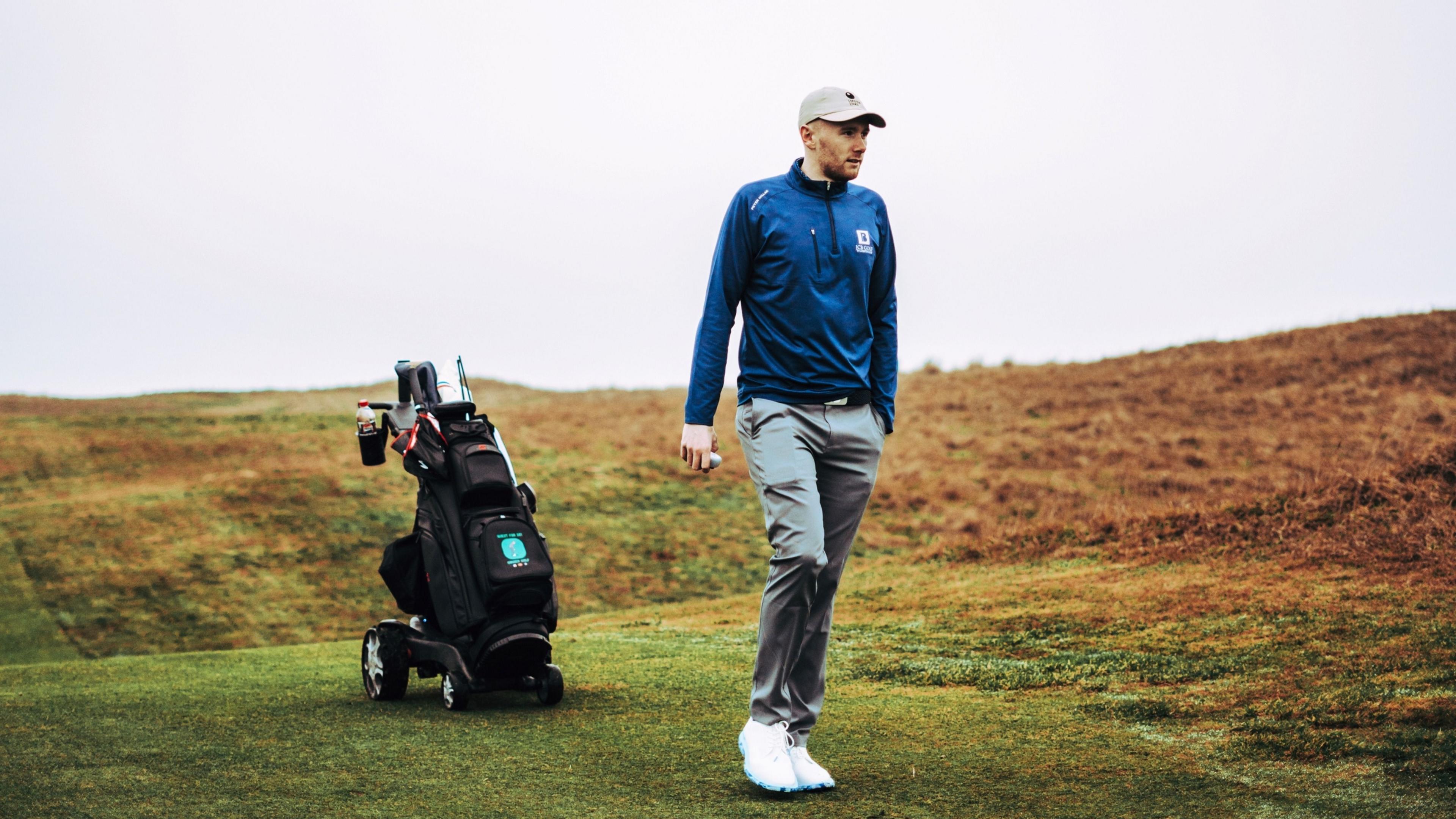 Golfer Josh Simpson on the fairway of a golf course with his buggy behind him.