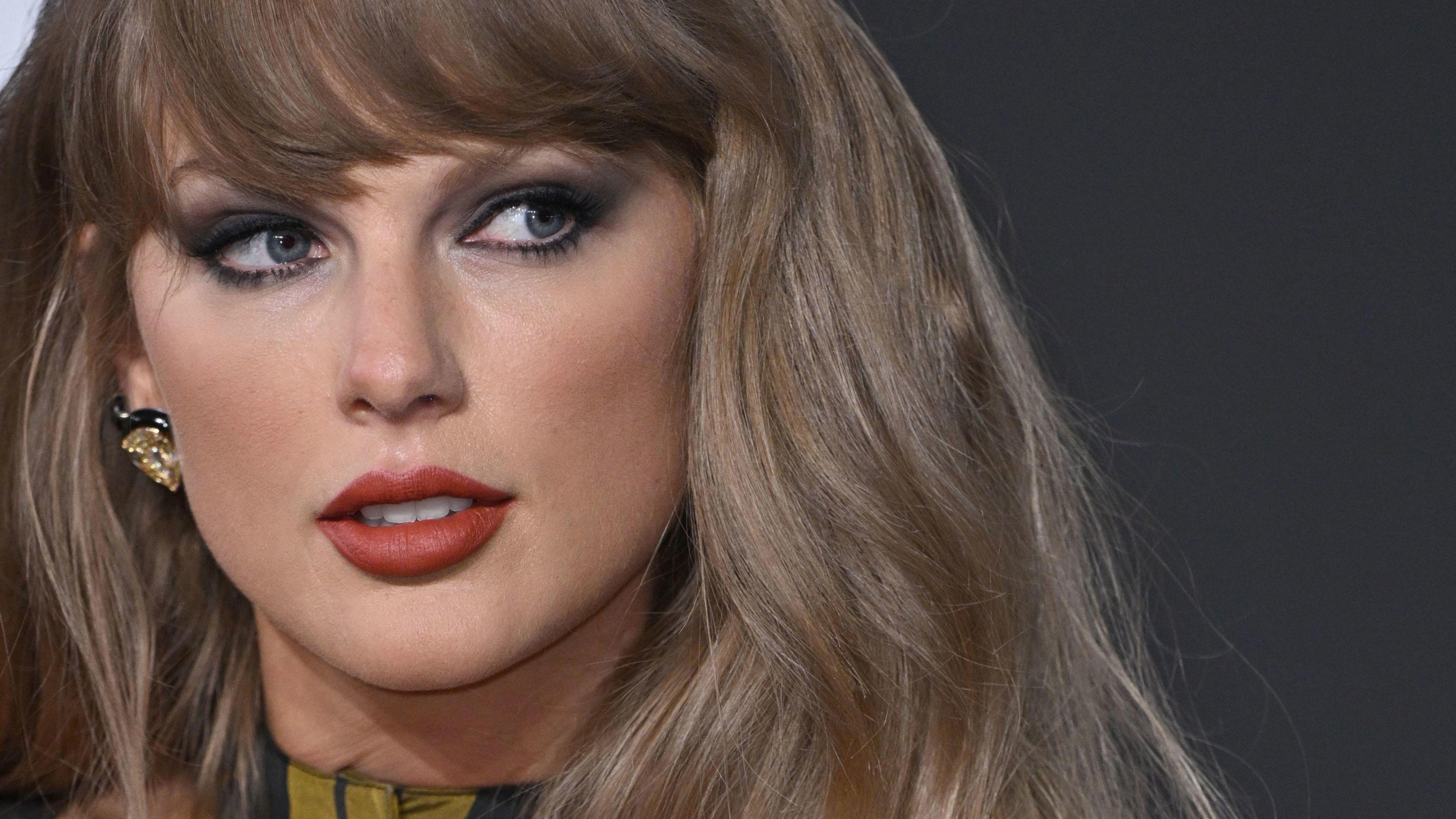 Close up of pop star Taylor Swift. She has dark blonde hair and is looking to the side. She has eyeliner on and a berry colour lipstick.