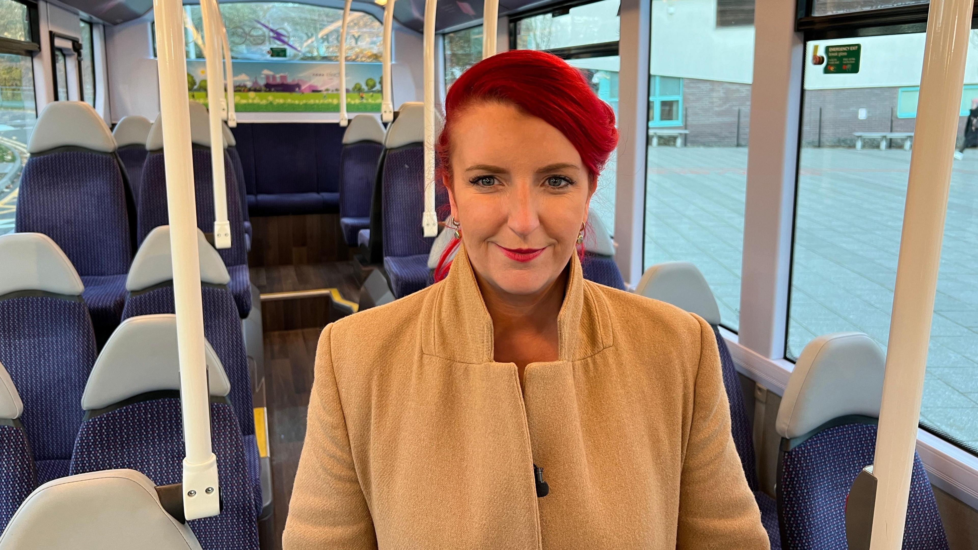 Transport secretary Louise Haigh stands on a bus outside York College. She is smiling, has crimson coloured hair and is wearing a camel-coloured coat.