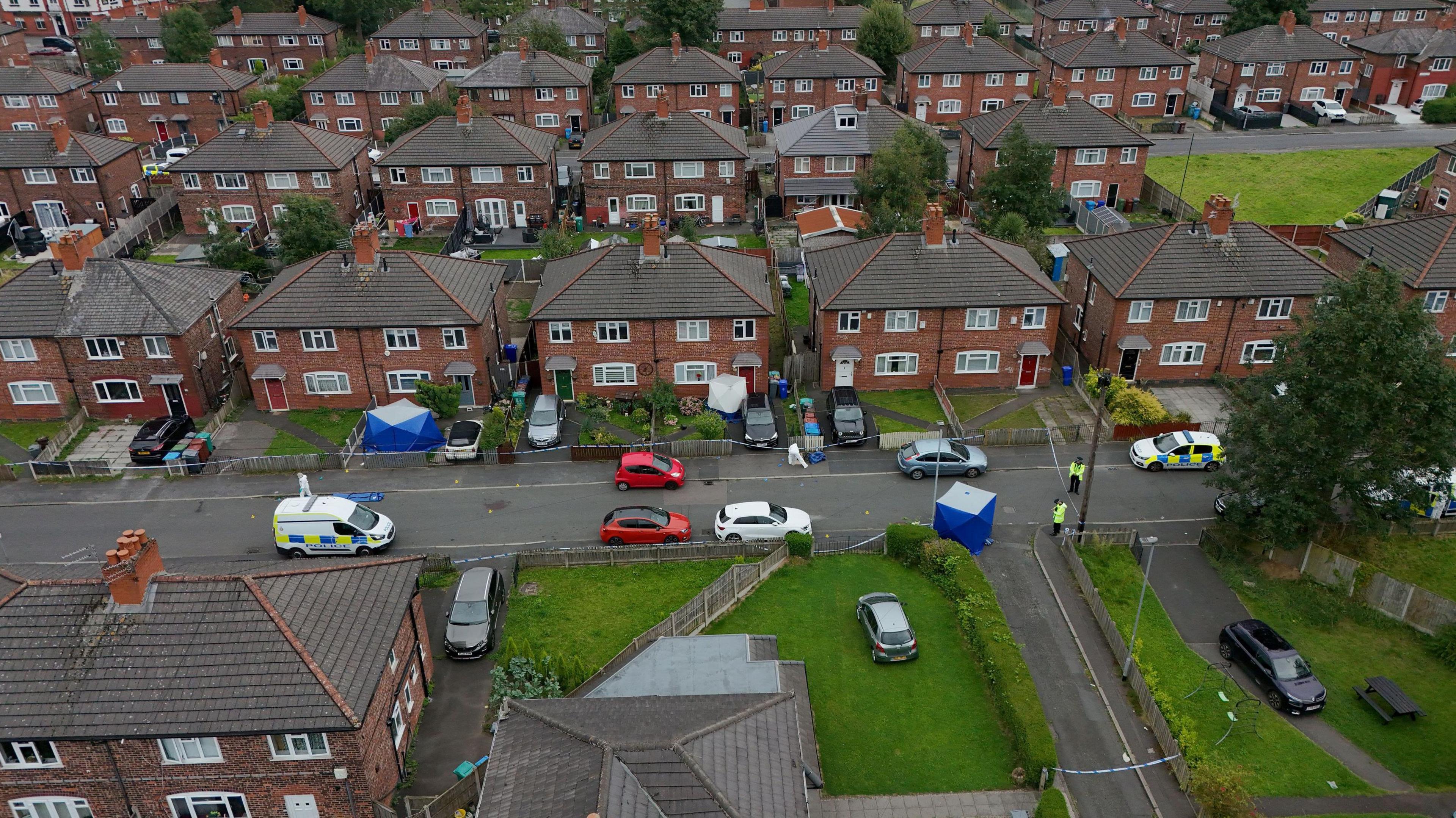 Overhead view of houses with police vans and forensic tents 