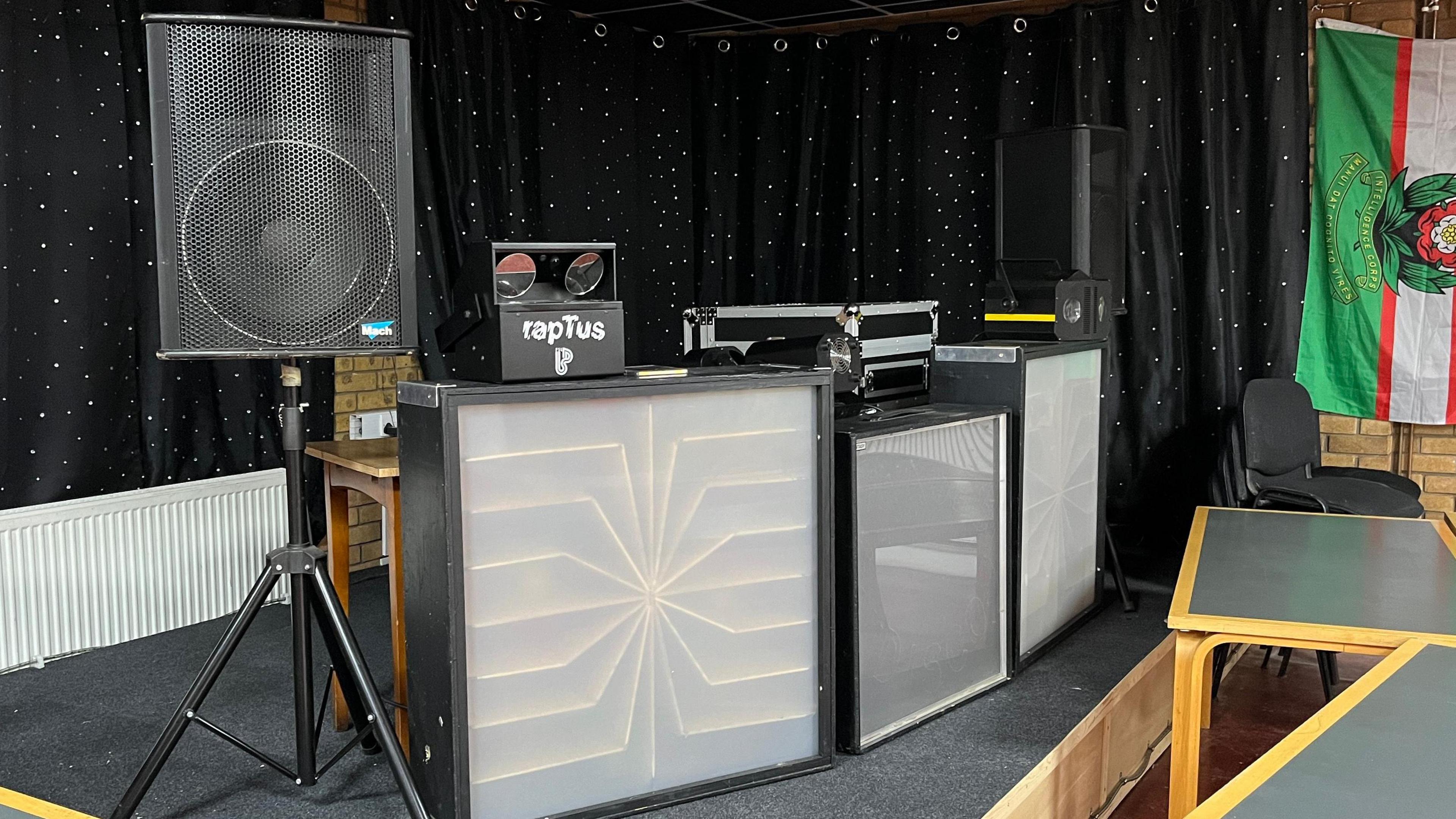 Speakers, lights and DJ equipment on a small indoor stage. 