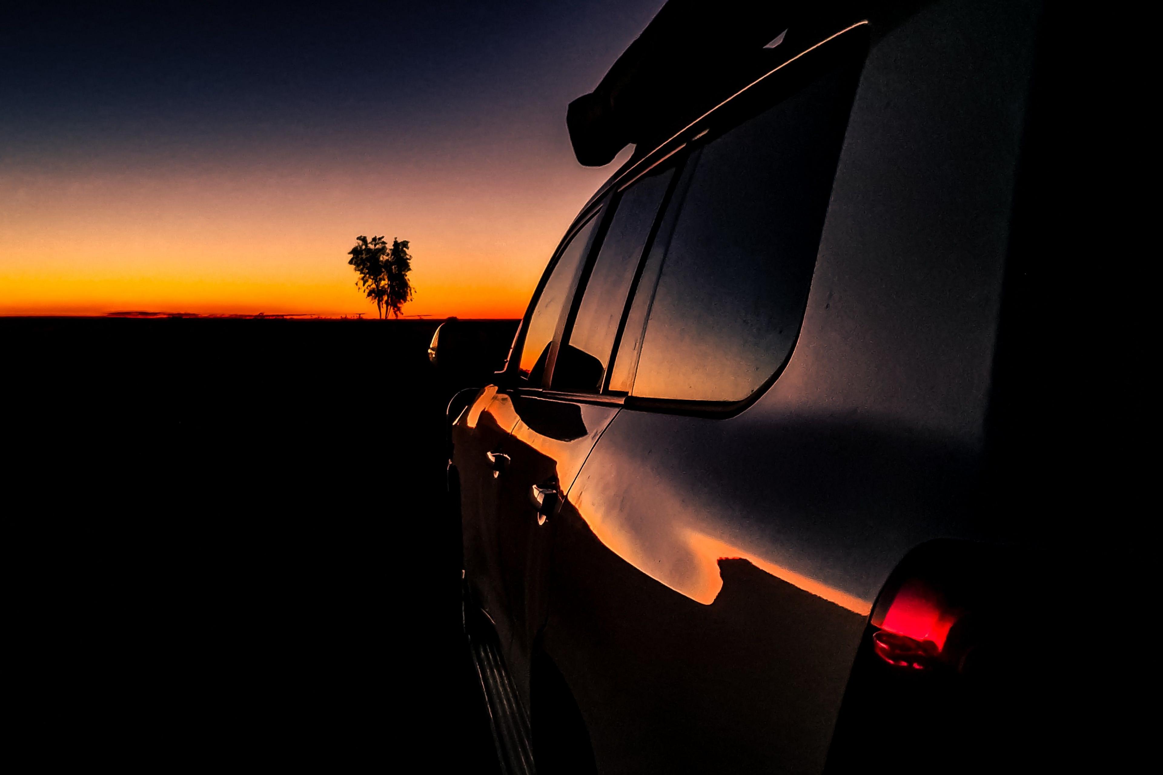 Sunlight reflects on the side of a car at dusk