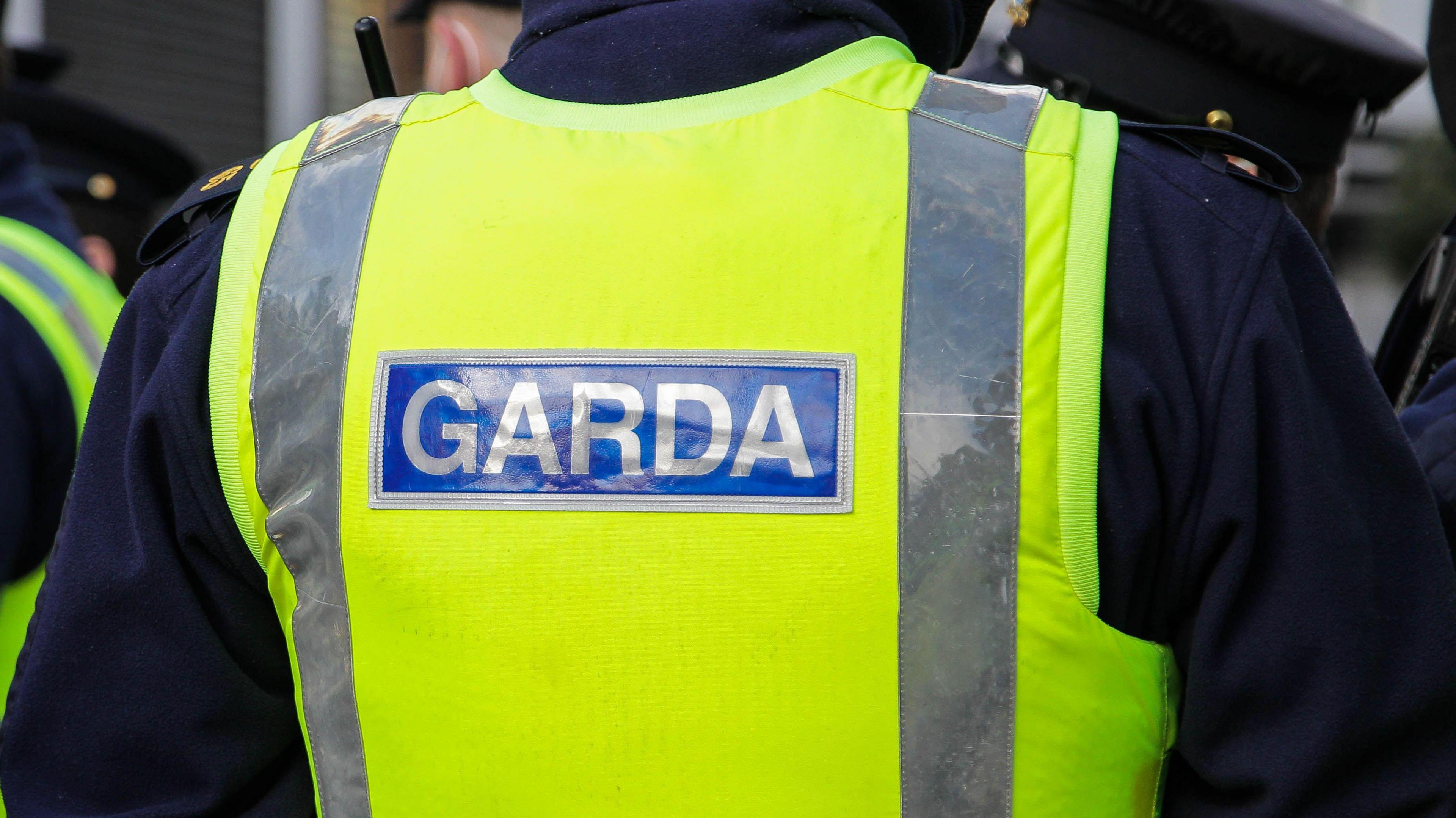 A gardai officer wears a yellow jacket with 'Garda' on the back in grey writing and blue background