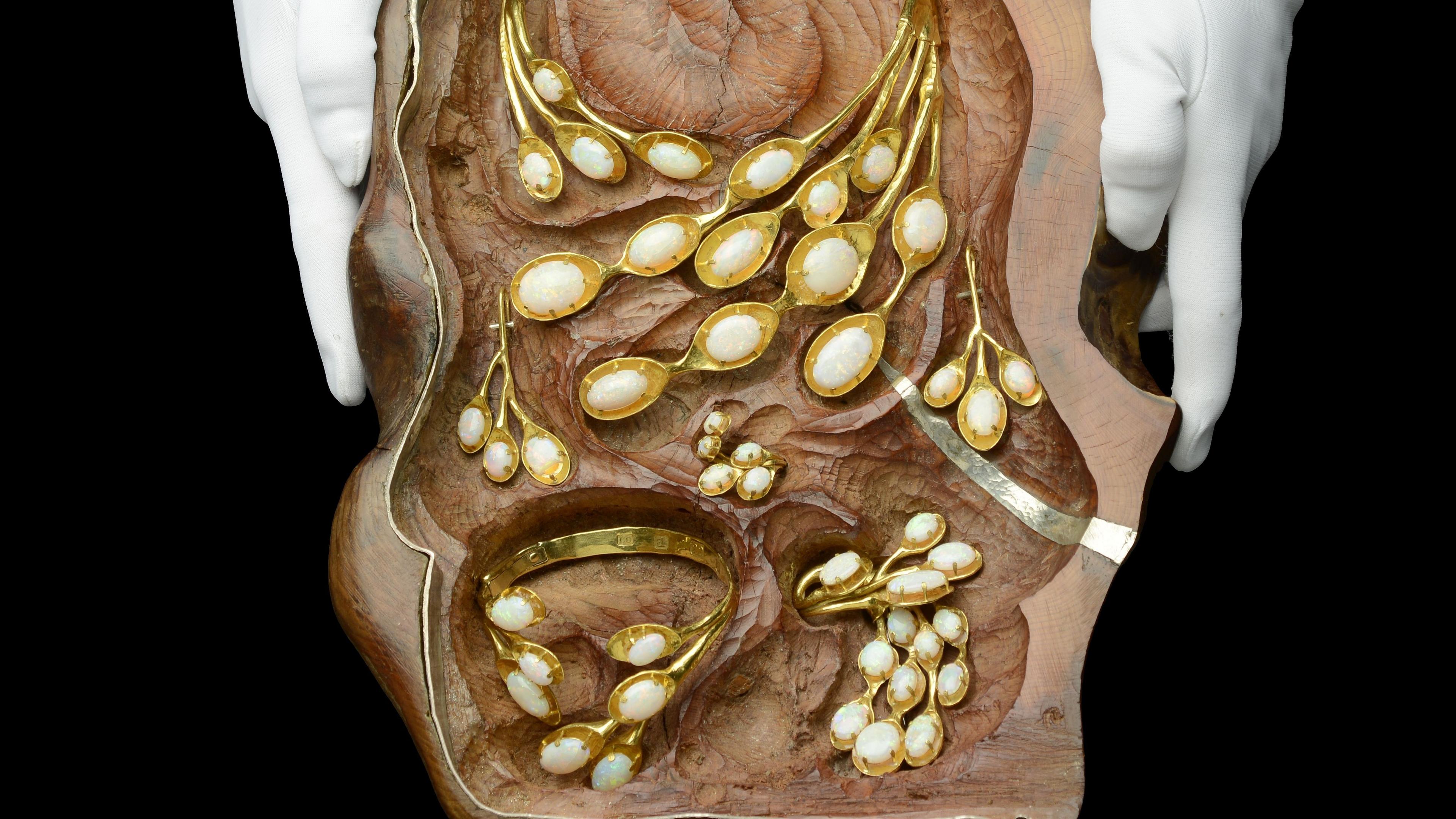 Two white glove hold a hollowed out wooden case which contains a jewellery set of earrings, necklace, broach and bracelet all crafted in 22 carat gold. 