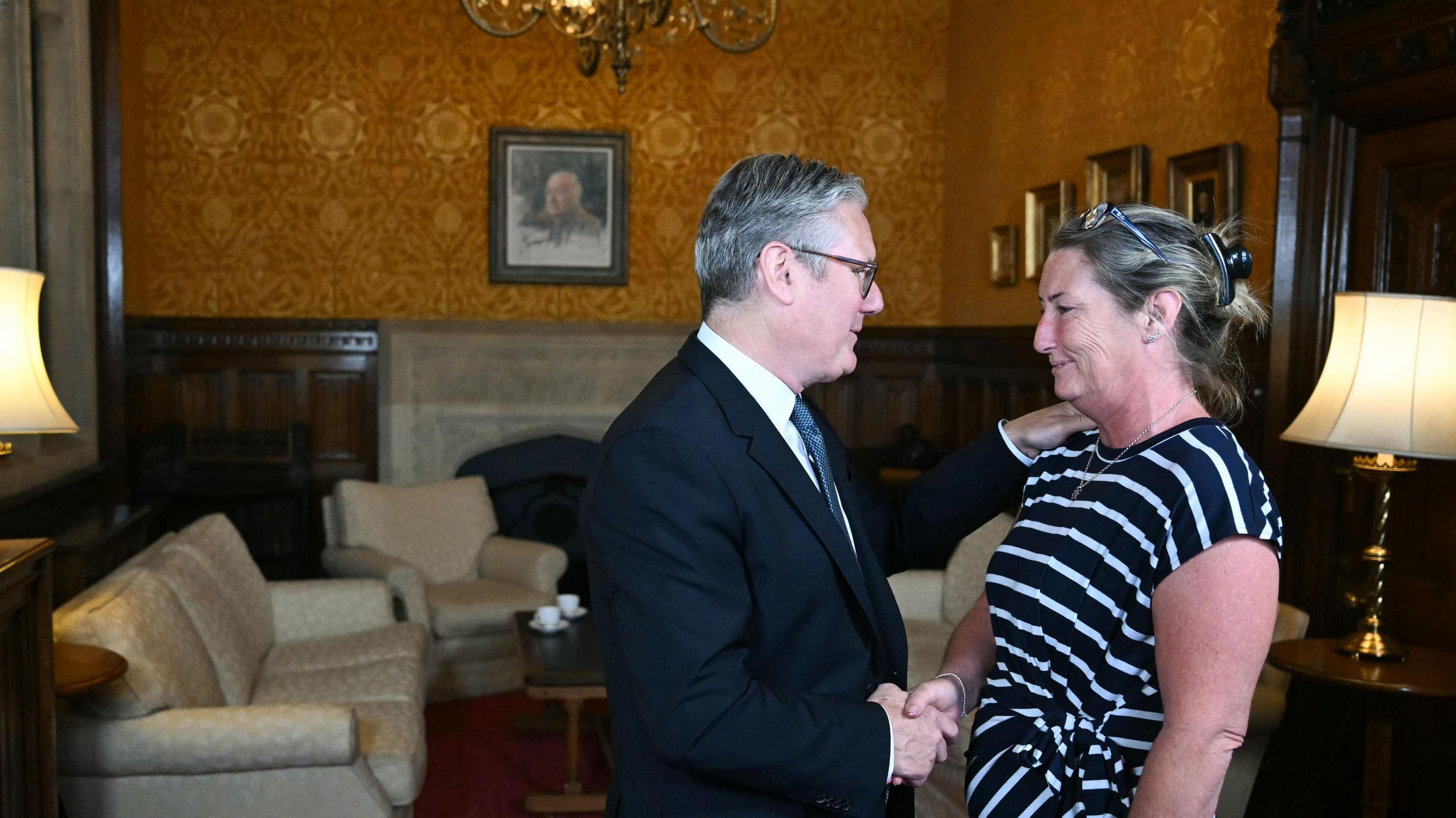 Sir Keir Starmer, who is wearing a dark suit, shakes the hand of Cheryl Korbel, who has blonde hair tied back and is wearing a black and white striped blouse.