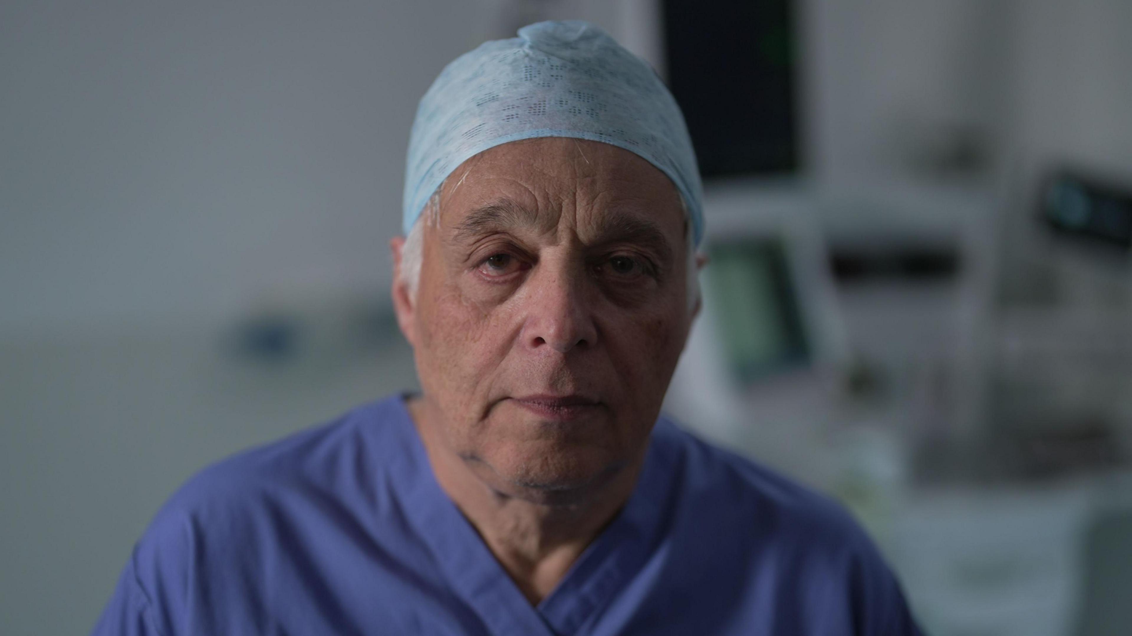 Consultant anaesthetist Richard Marks is photographed in a hospital environment, wearing his dark blue scrubs and pale blue surgeon's cap.