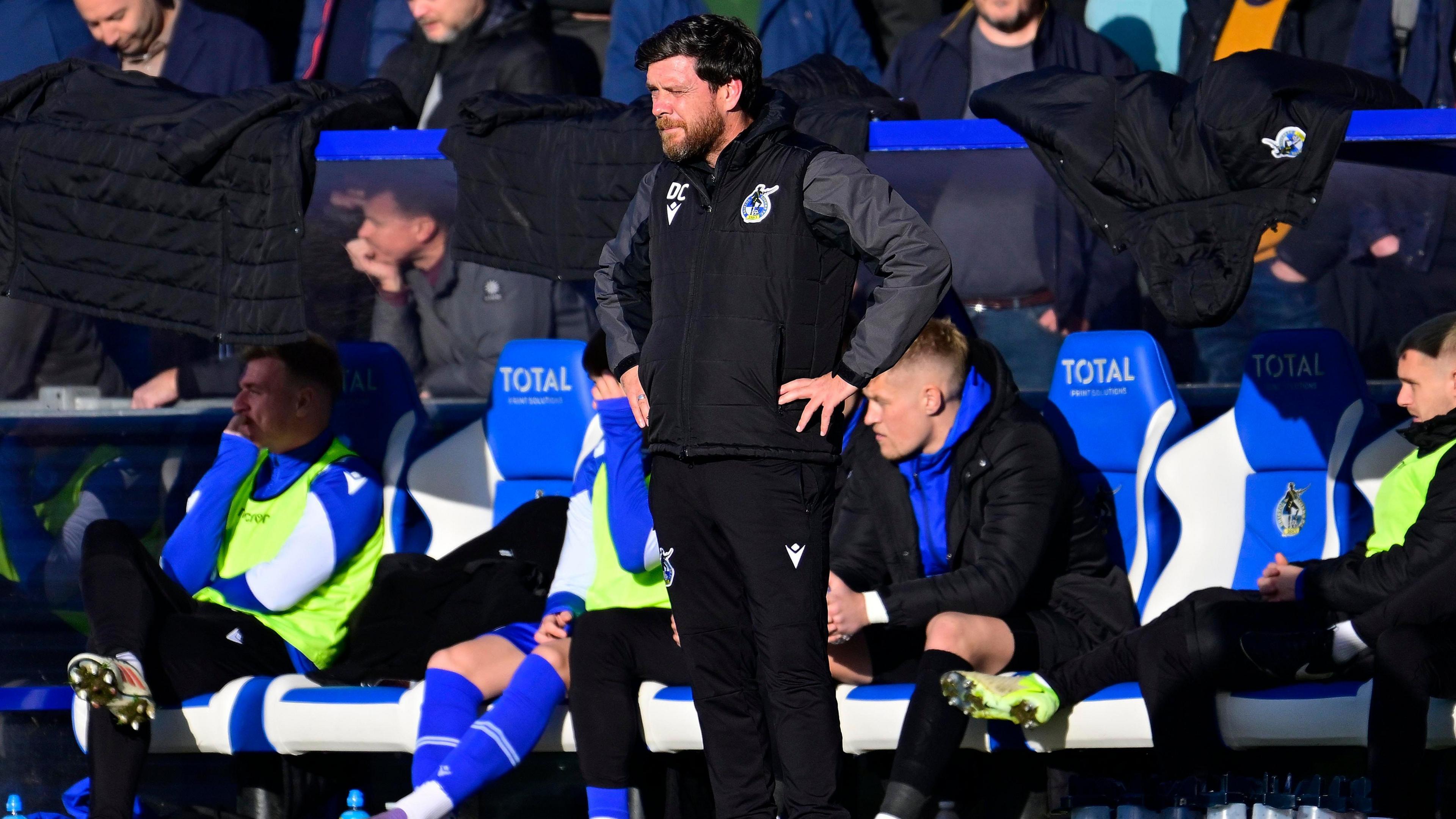 Darrell Clarke stands in the dugout with his hands on his hips as he watches the match 