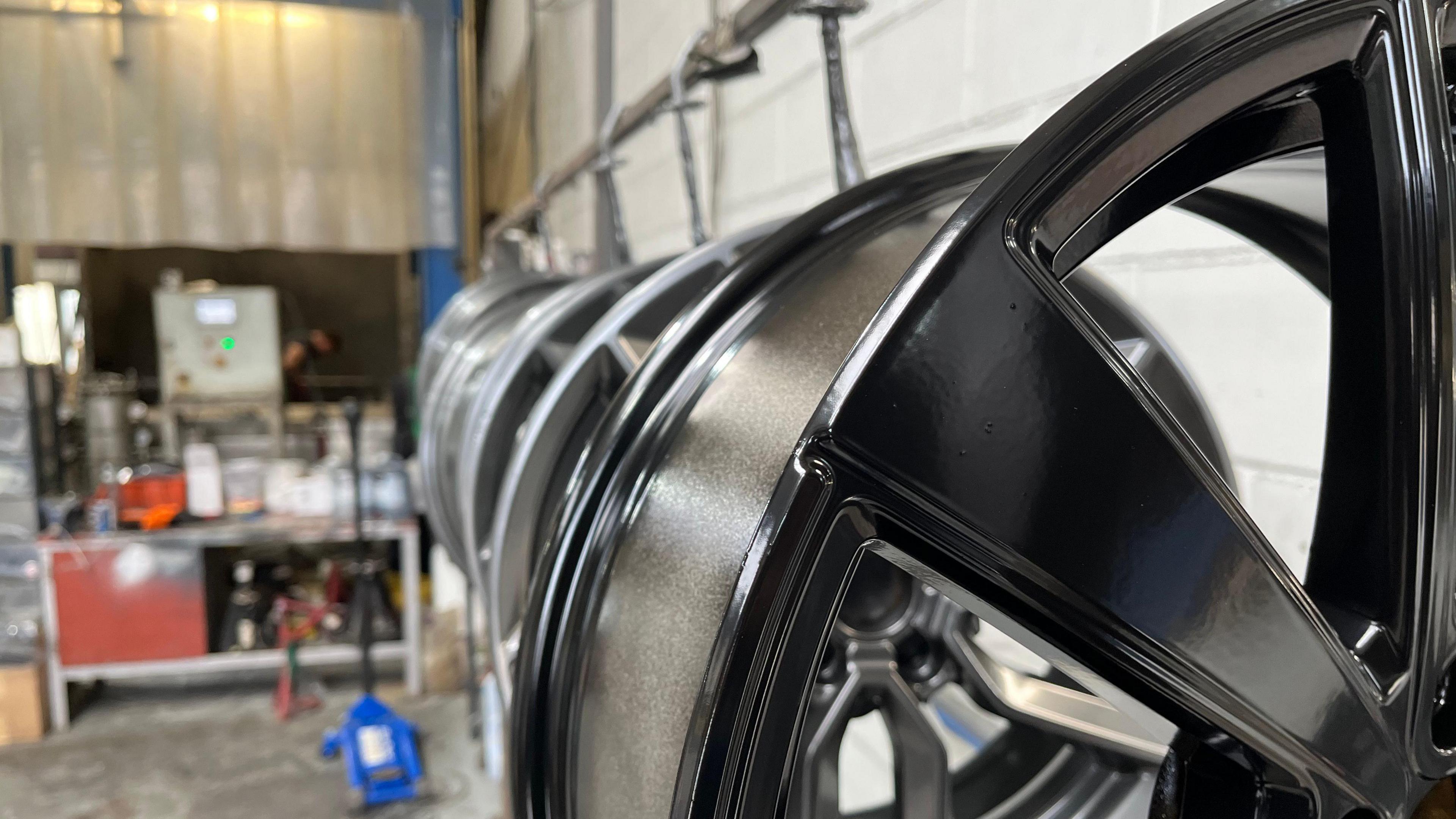 A row of painted silver alloy wheels, hung up in a garage workspace. 