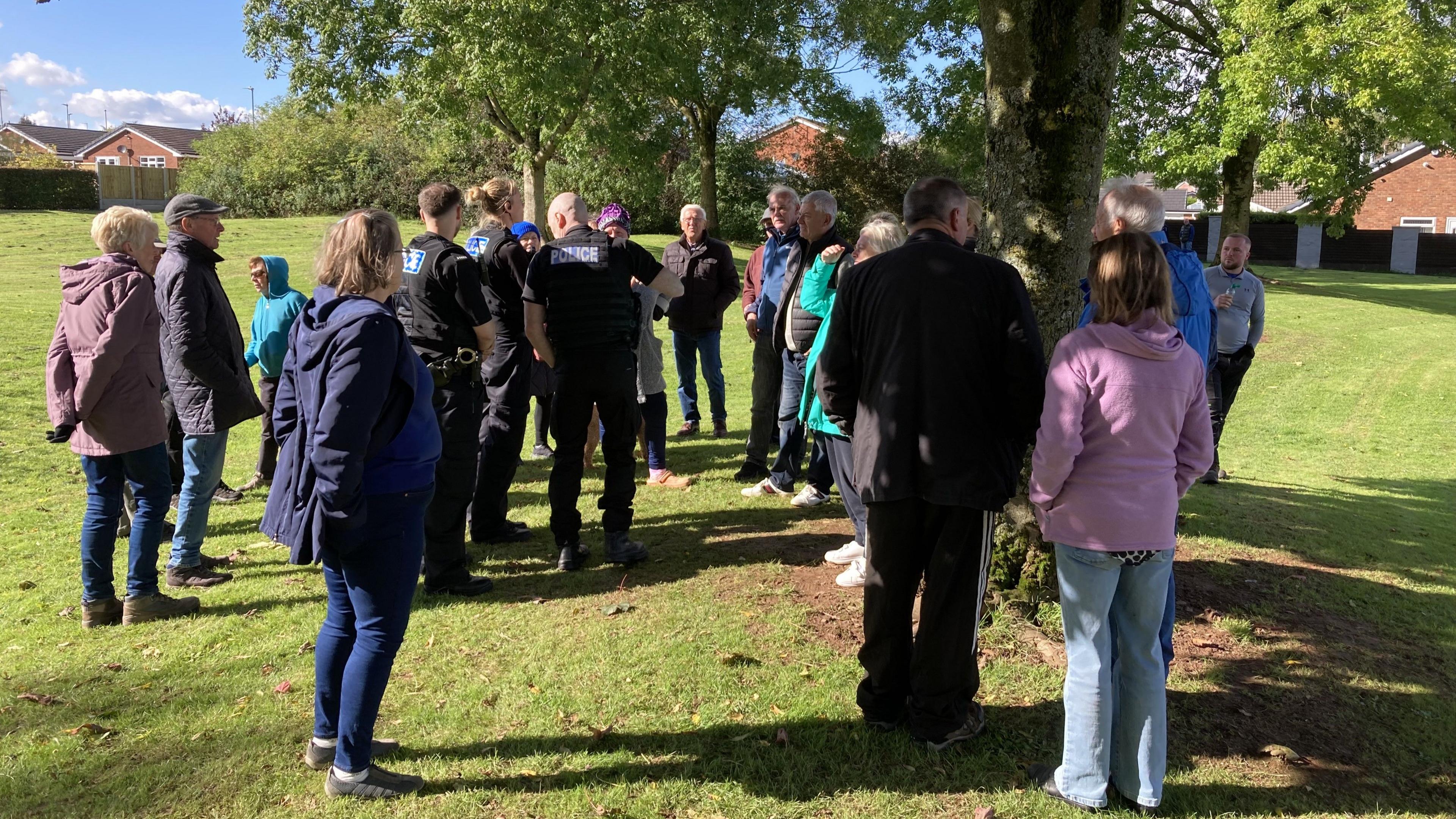 A group of people gathered around some trees, with three police officers in the middle of the crowd