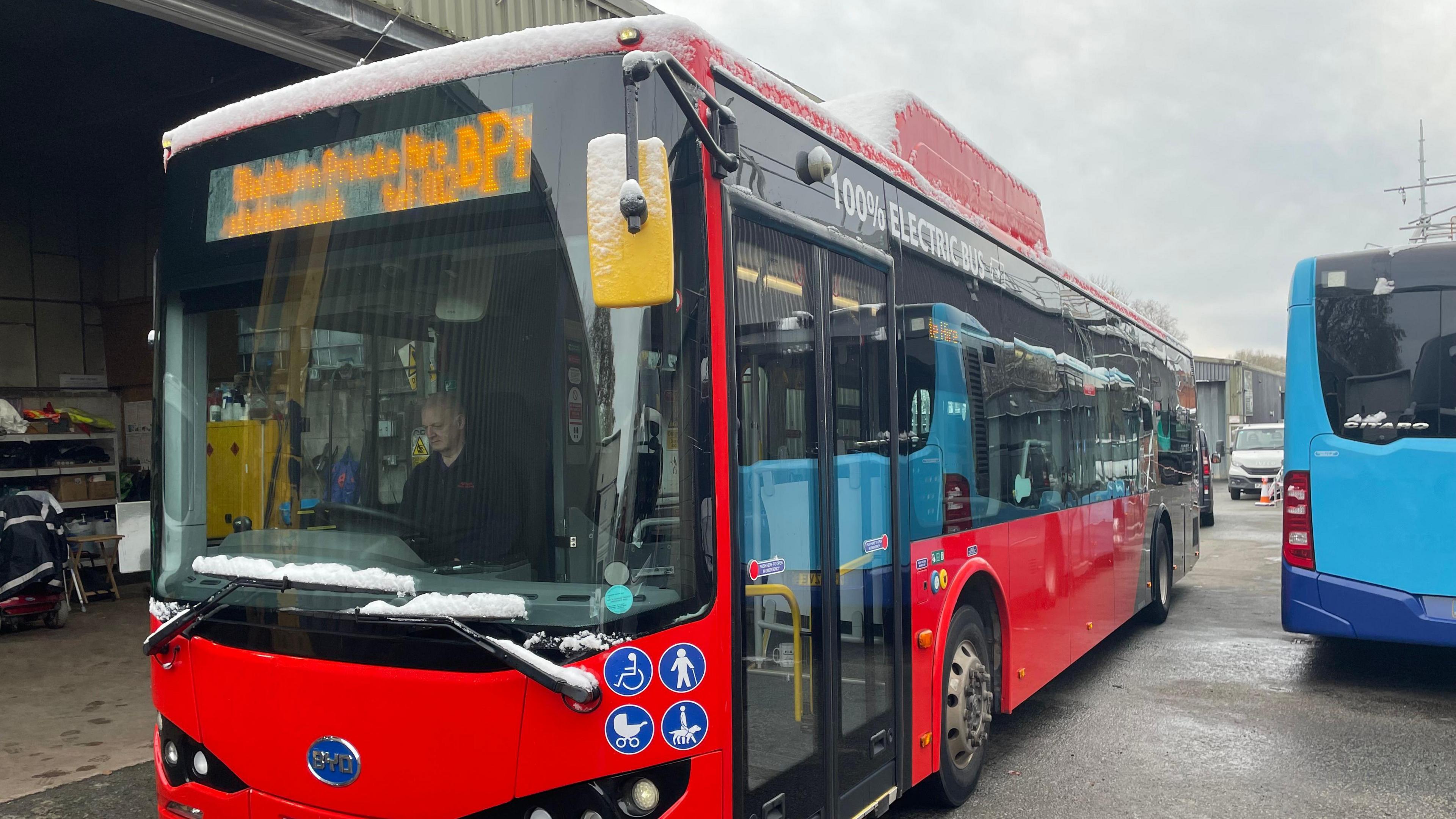 single-decker red bus being driven past a blue bus on a Blackburn road