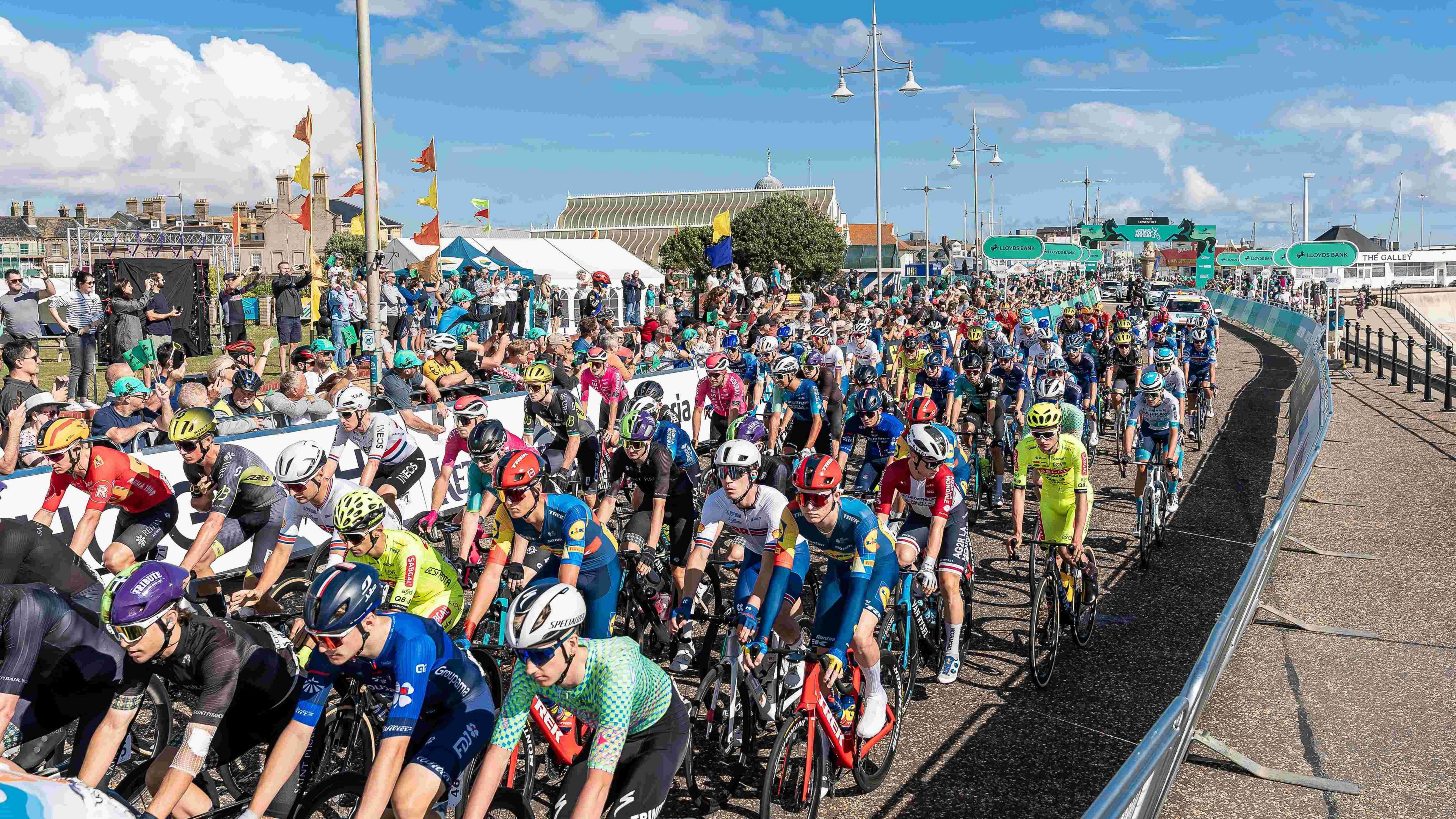 Hundreds of cyclists ride near Lowestoft beach front during the Tour of Britain cycle race. Spectators watch from the left hand side.