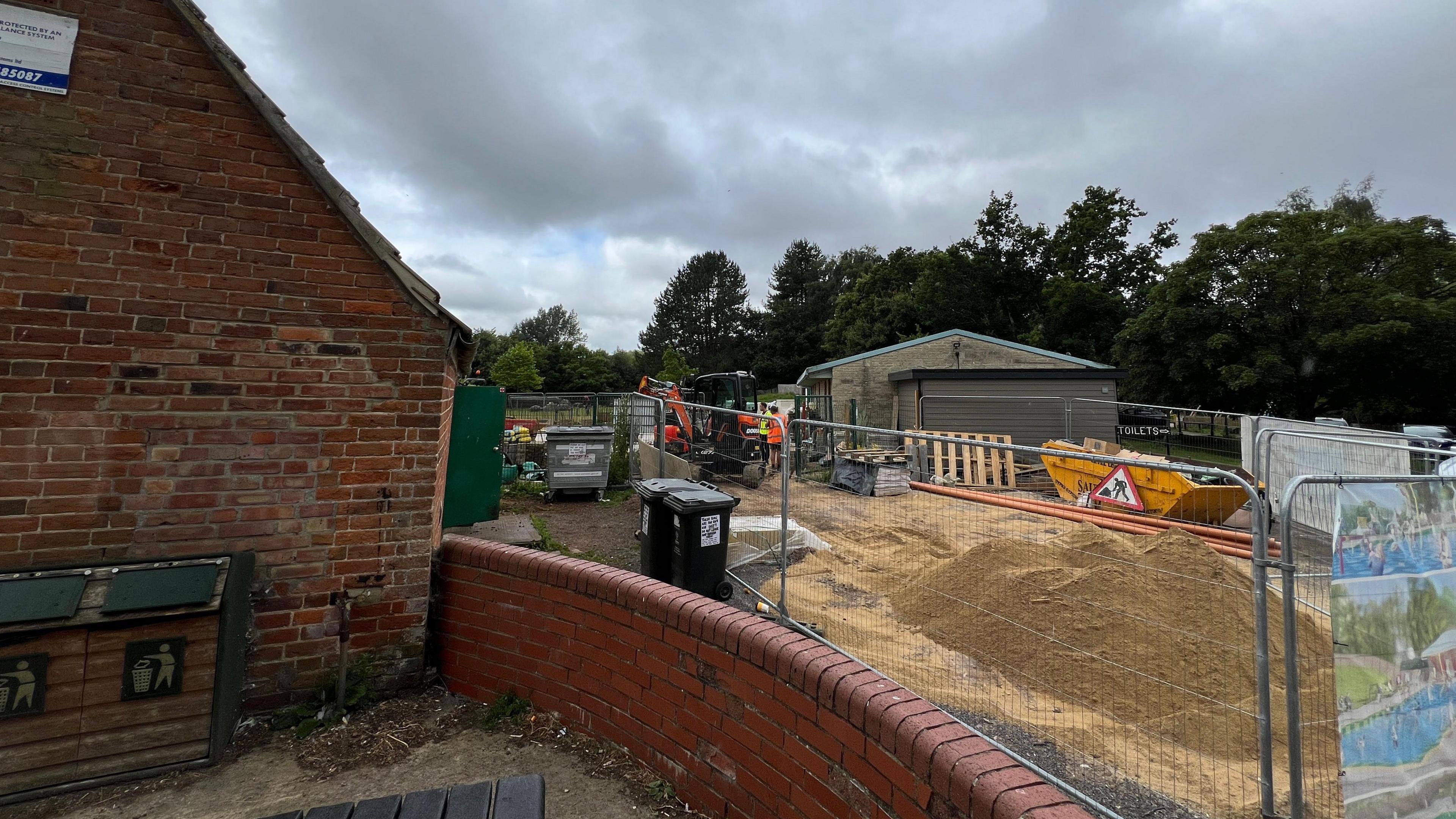 Building site behind a red brick wall and a wire building site fence 