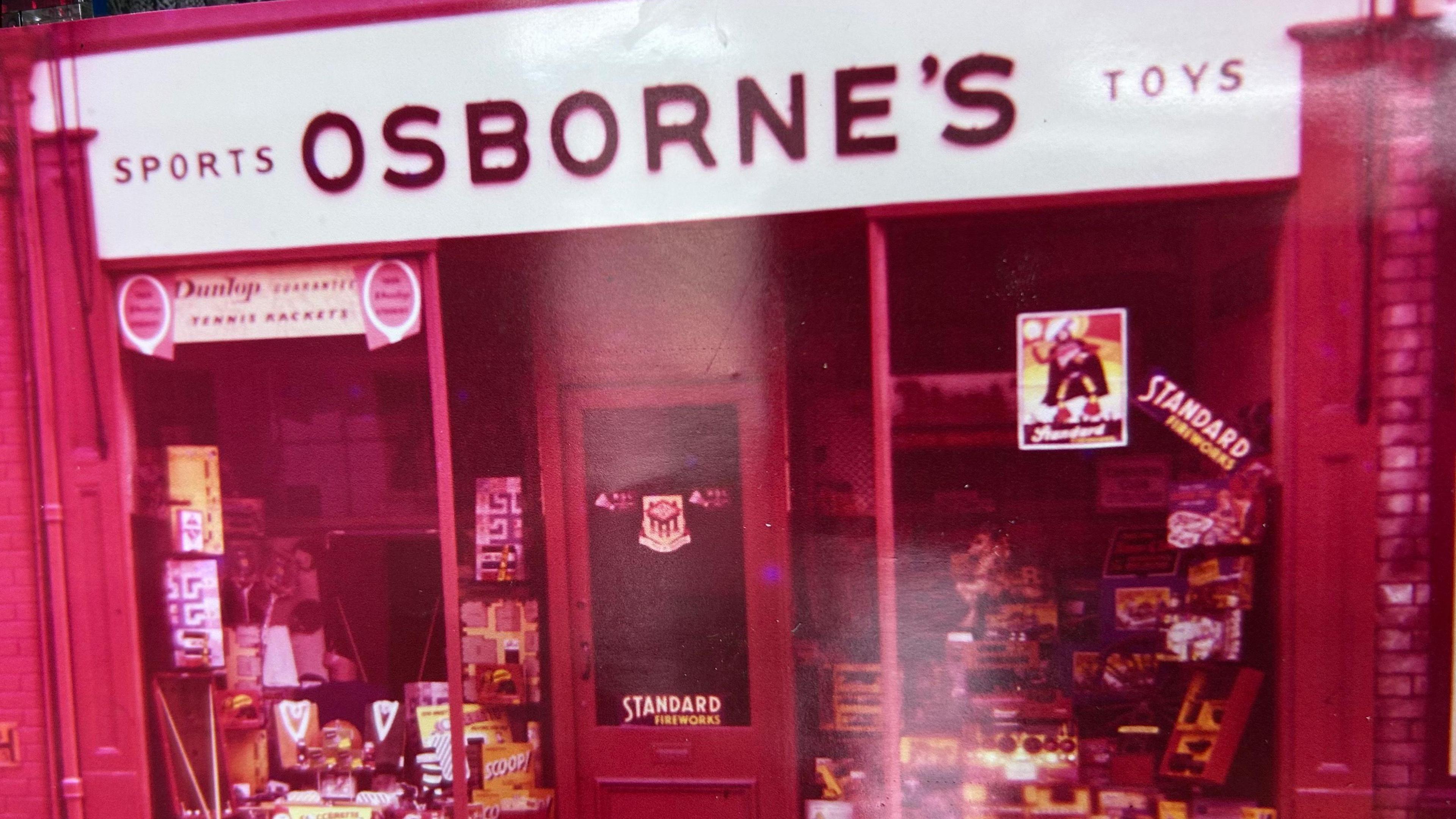 A photo of a toy shop with a red tint. A large white sign reading "Sports, Osborne's toys" is above the entrance.
