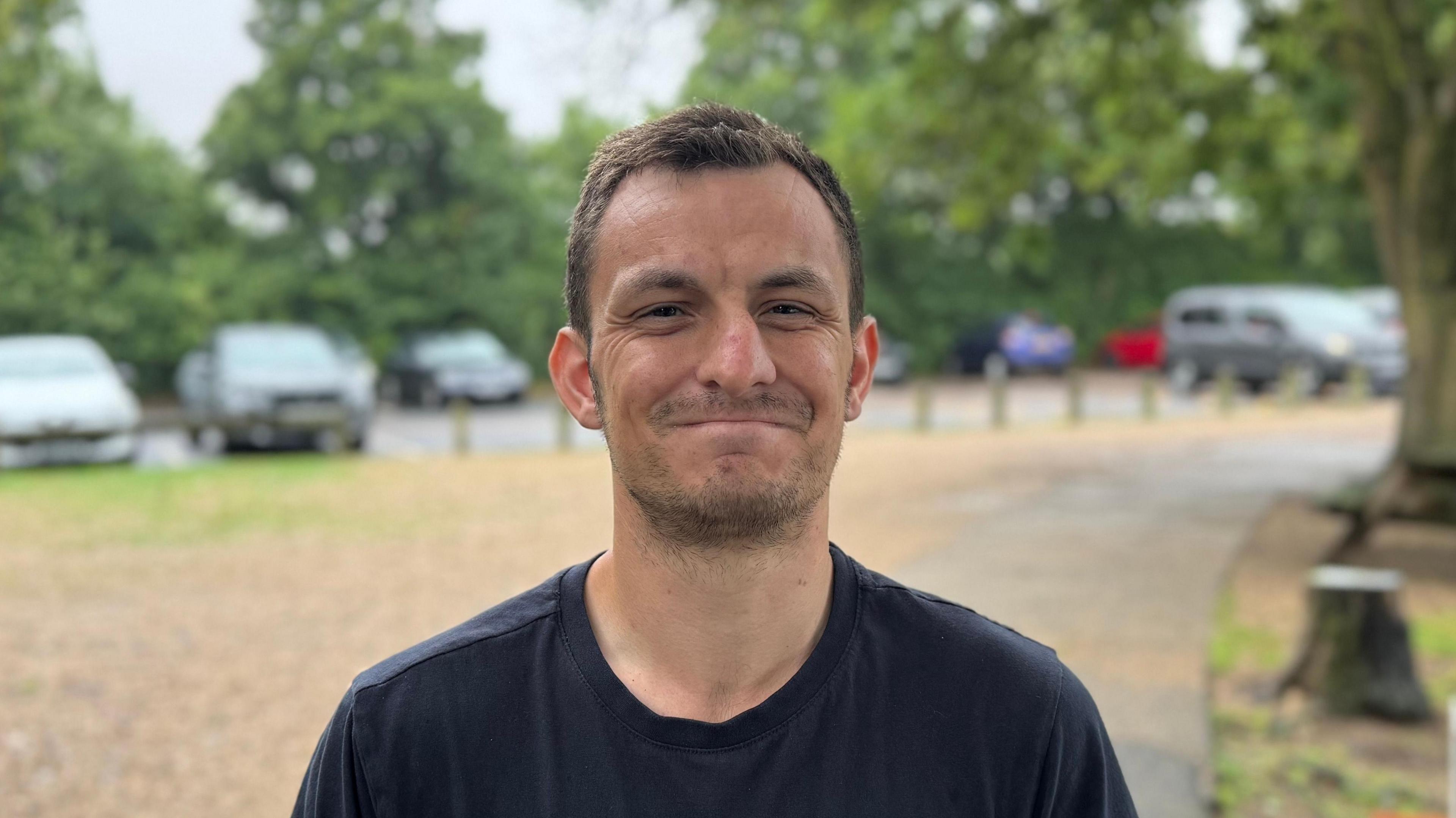 A head and shoulders image of Luke Wells. He is wearing a black T-shirt. He is looking directly into the camera. 