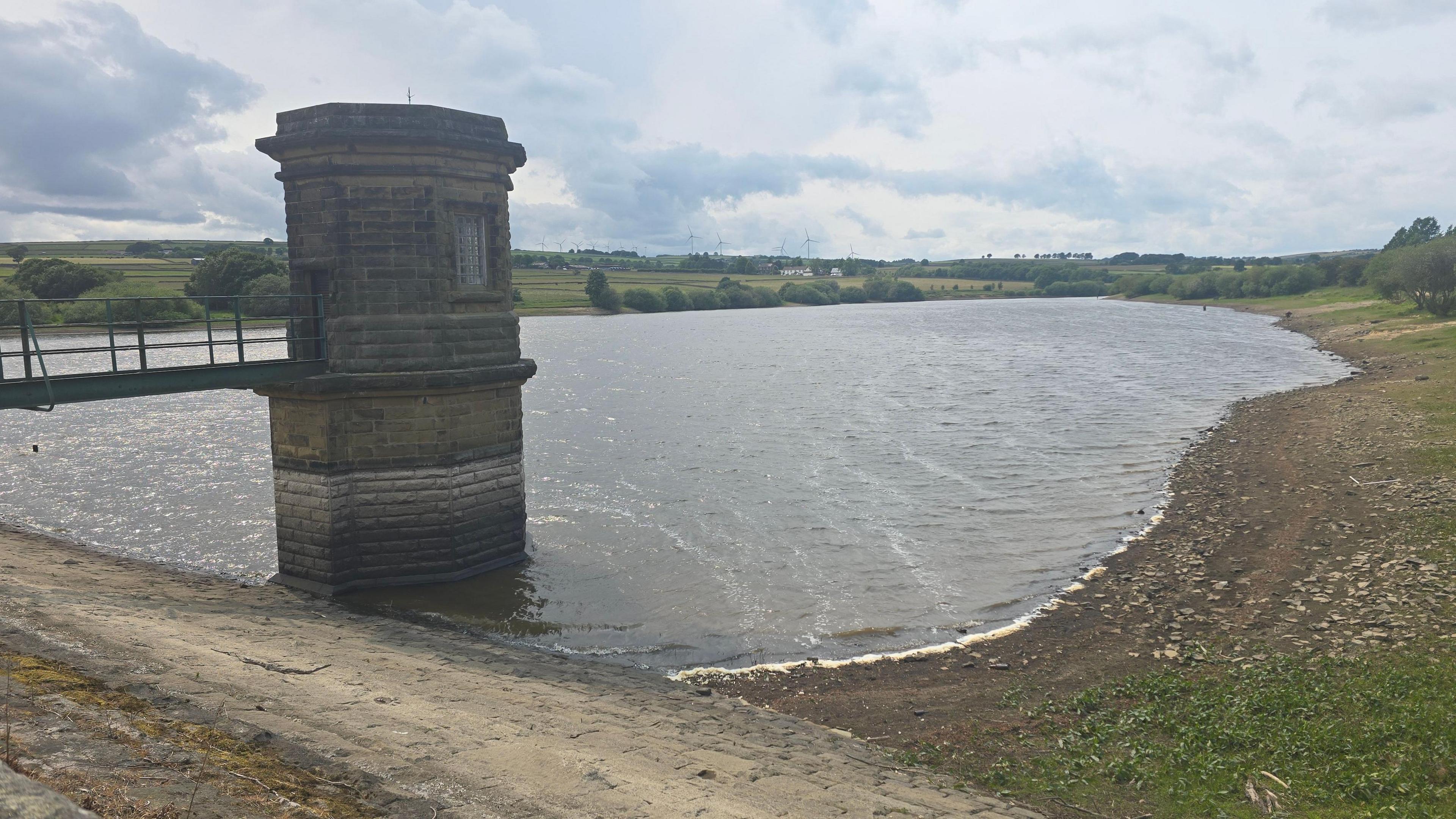 A reservoir with a small brick tower and metal bridge leading to it