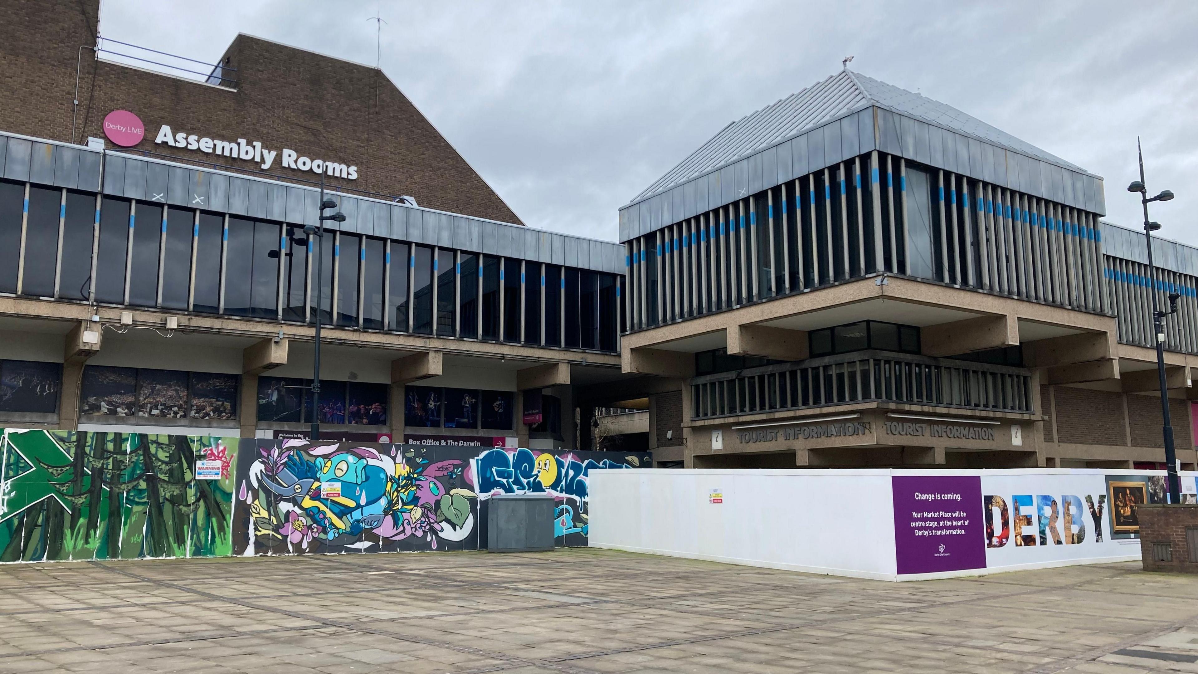 A photograph of the outside of The Assembly Rooms in Derby - it's an events space with lots of glass windows and boarding around the edge with graffiti on