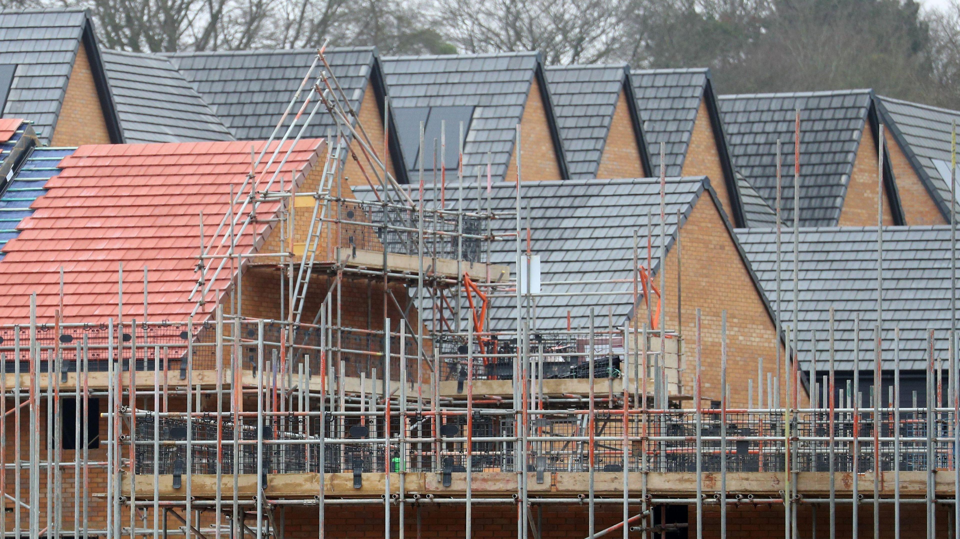 Generic shot of a building site where houses are being constructed. Tiled roofs can be seen as well as lots of scaffolding
