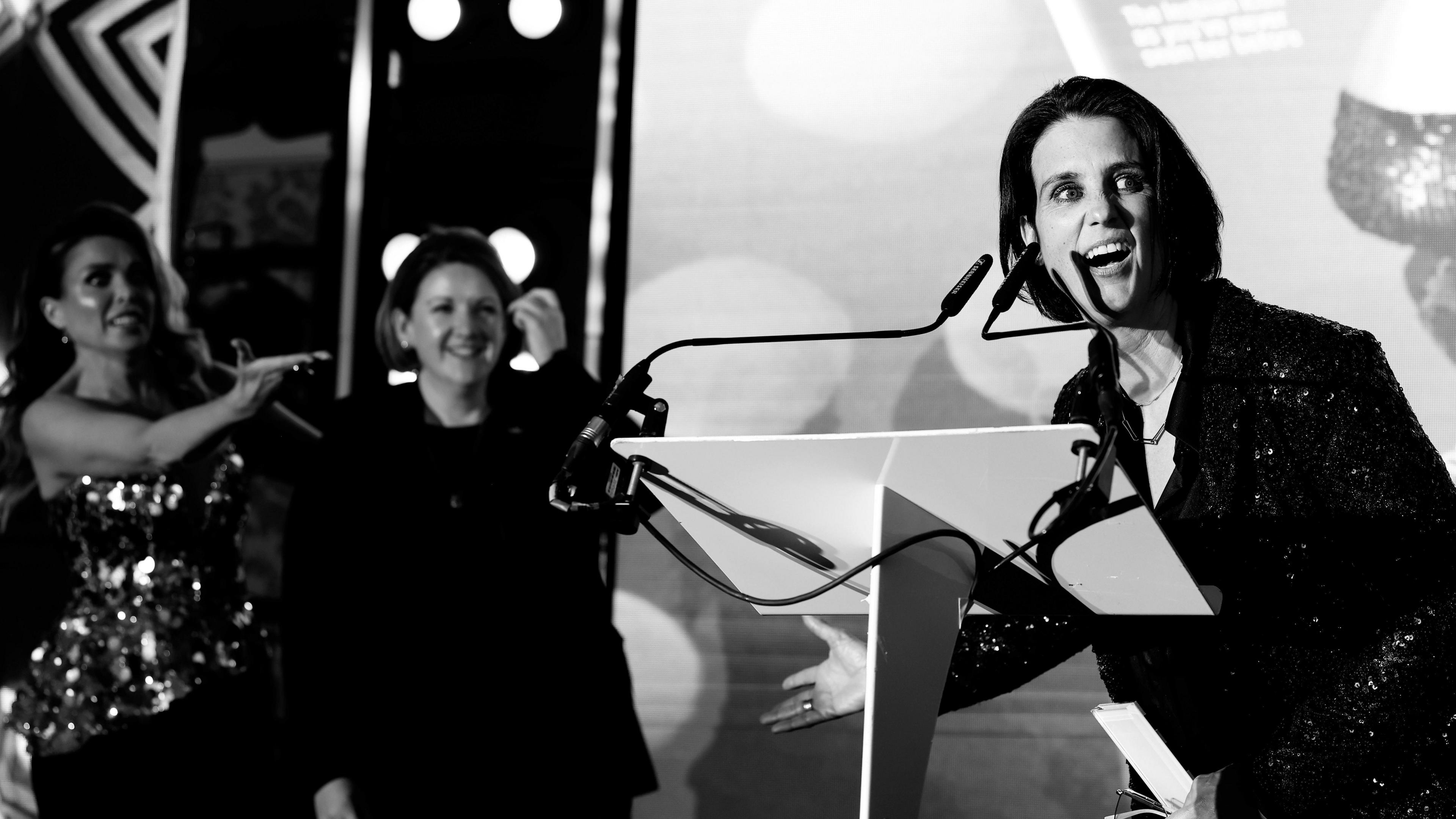 Heather Peace with the 30 Years of Diva Award during the DIVA Awards 2024 at Grand Connaught Rooms on April 26, 2024 in London, England. She is wearing a dark suit and standing at a lectern speaking into a microphone, as two other women watch on from the side of the stage.