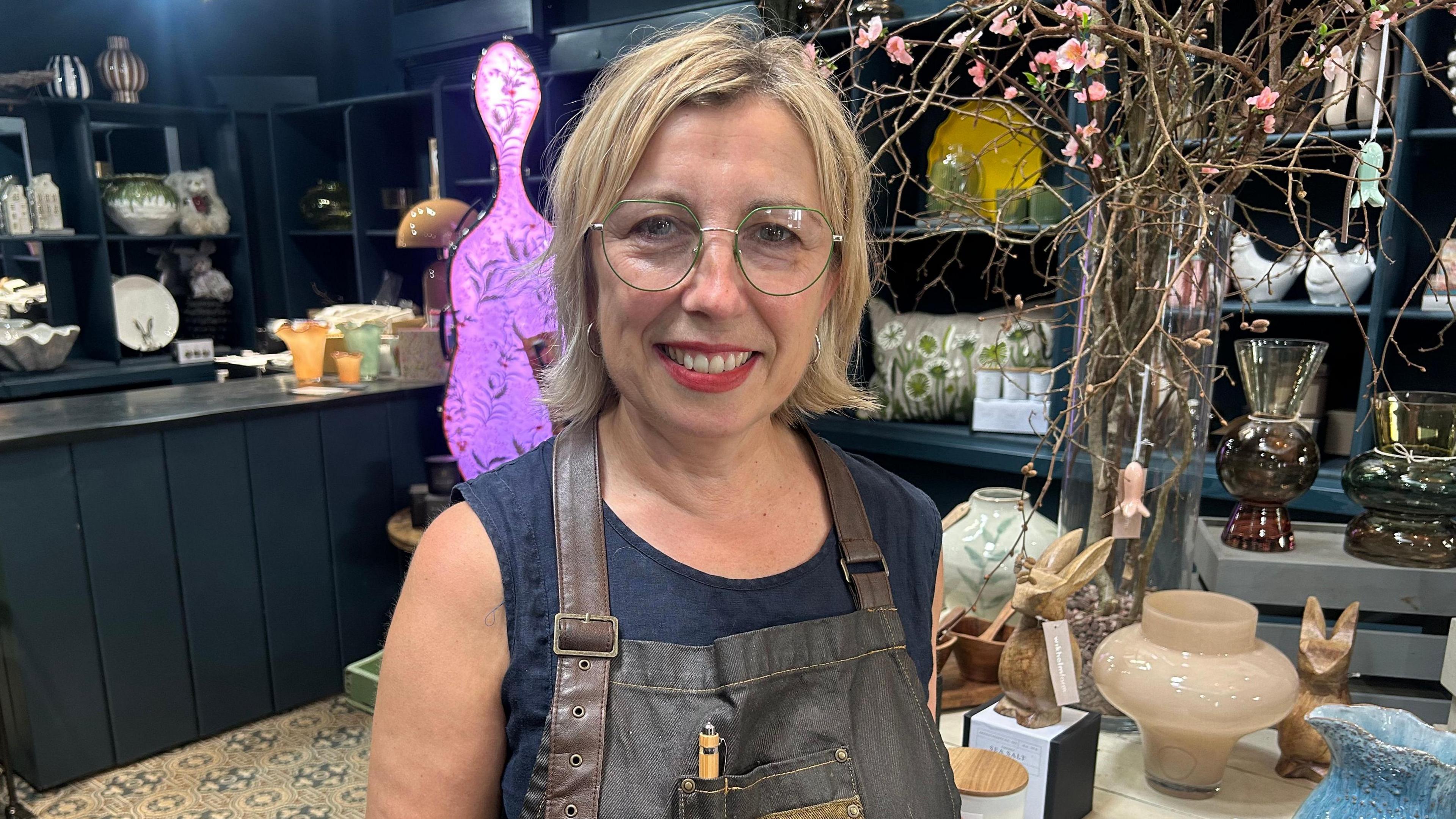 Gabrielle Davies yn gwenu a phwyso ar fwrdd yn ei siop yn nhref Llanbed 