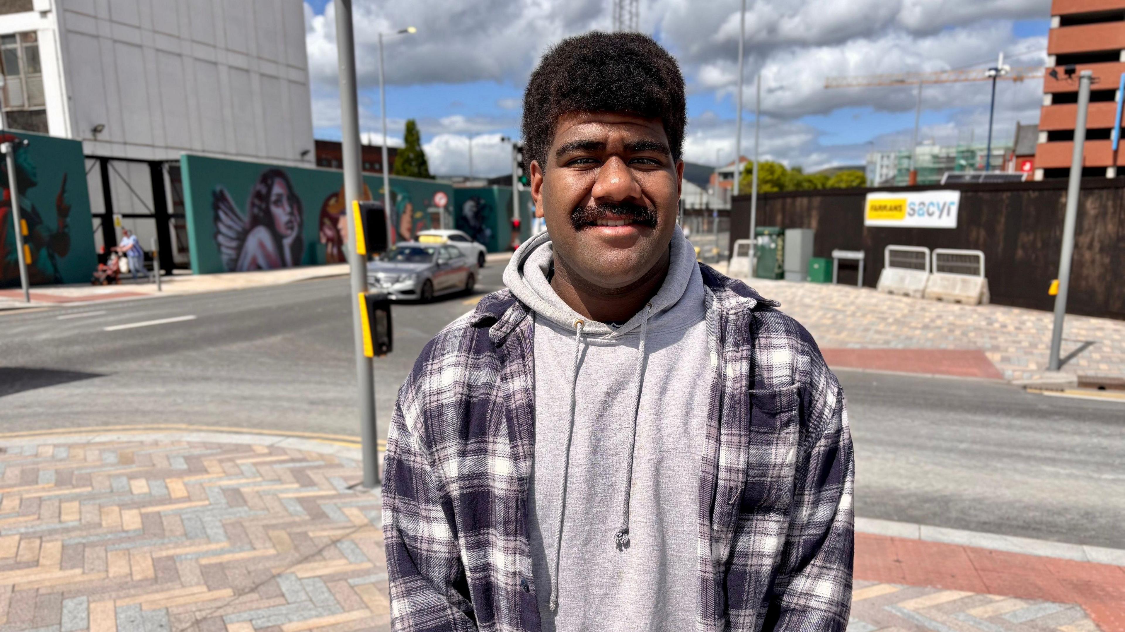 Livai Naga. He has think black hair and moustache, wearing a check shacket with grey hoodie.