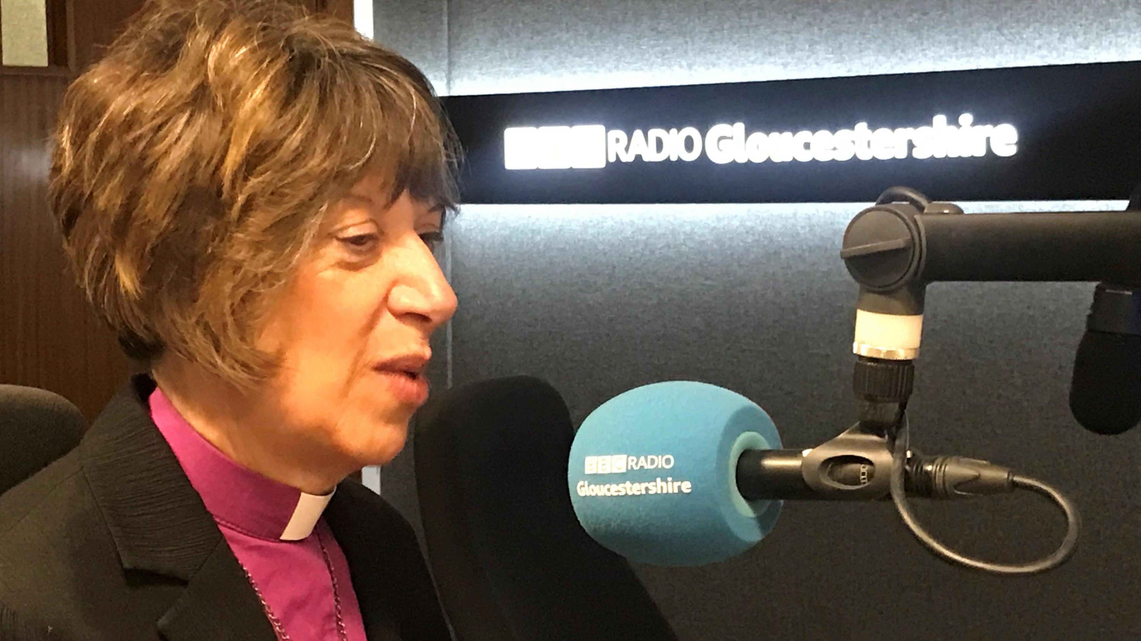 Bishop Rachel Treweek in a radio studio with a sign reading "BBC Radio Gloucestershire" in the background