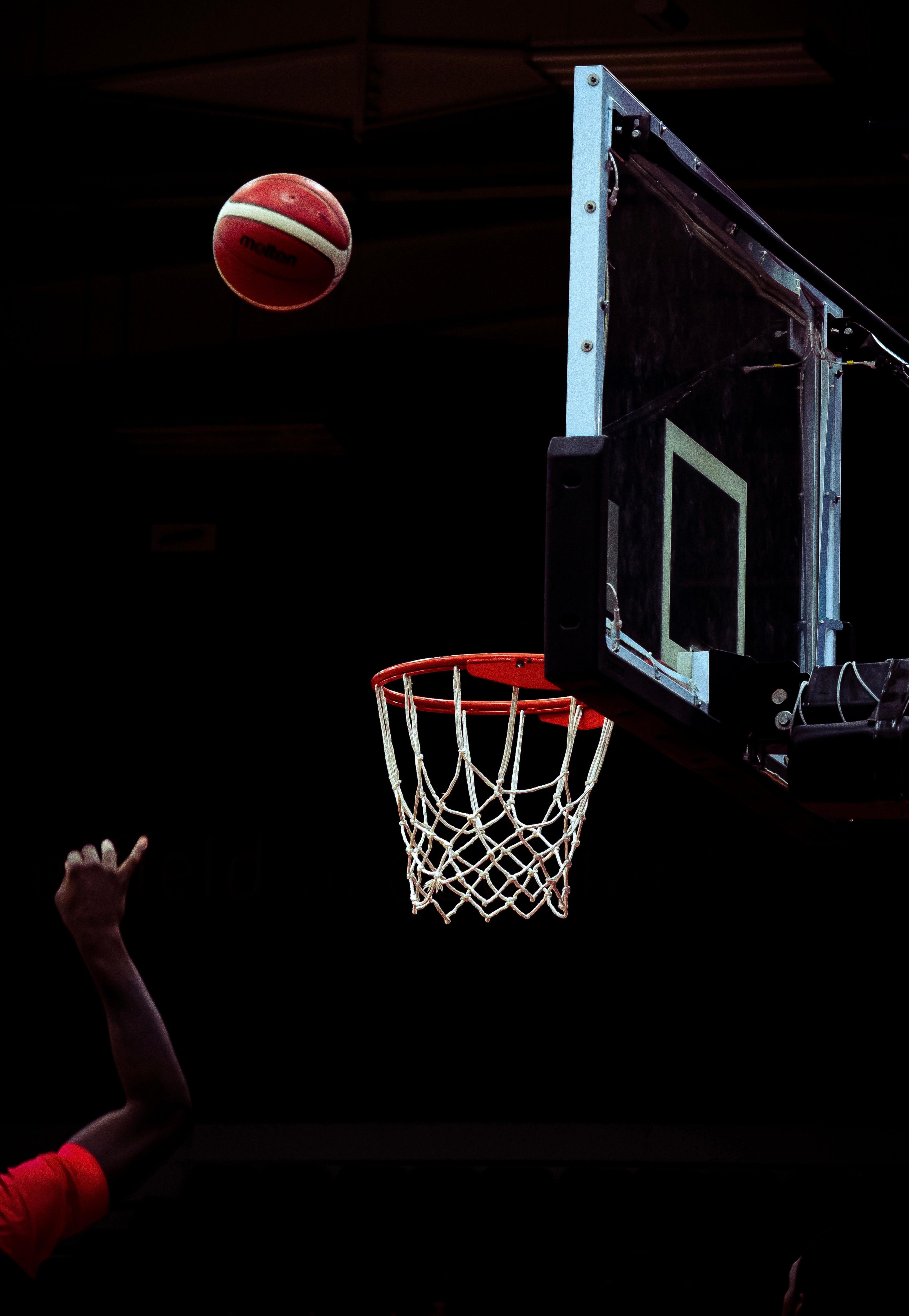 Red and white ball thrown mid air, aiming to go in a basket ball hoop 