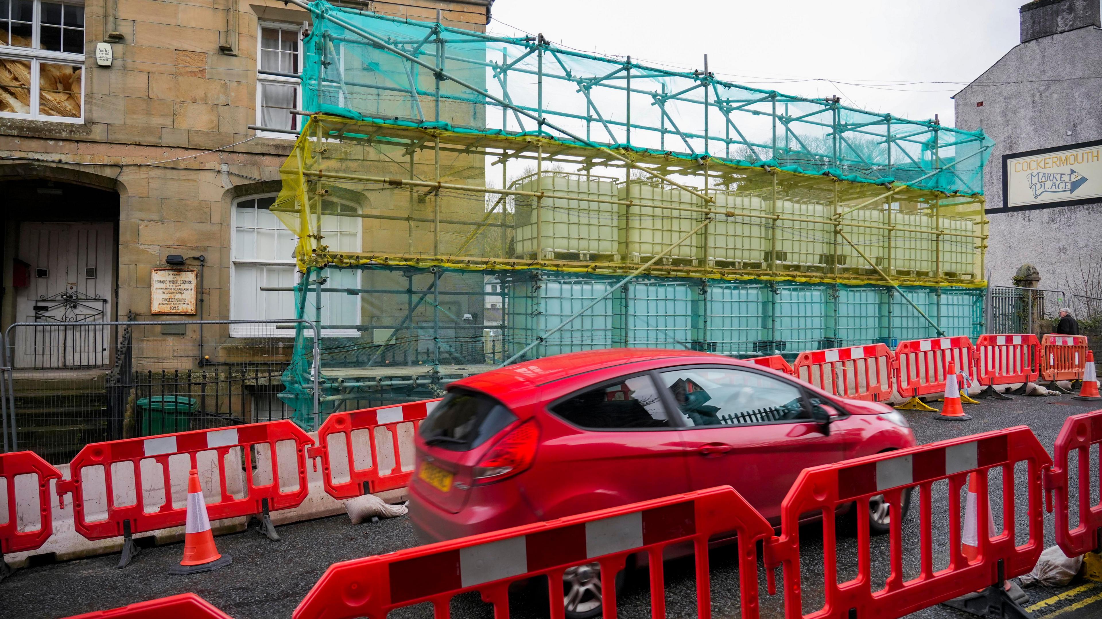 Car about to cross Cocker Bridge with scaffolding and net behind