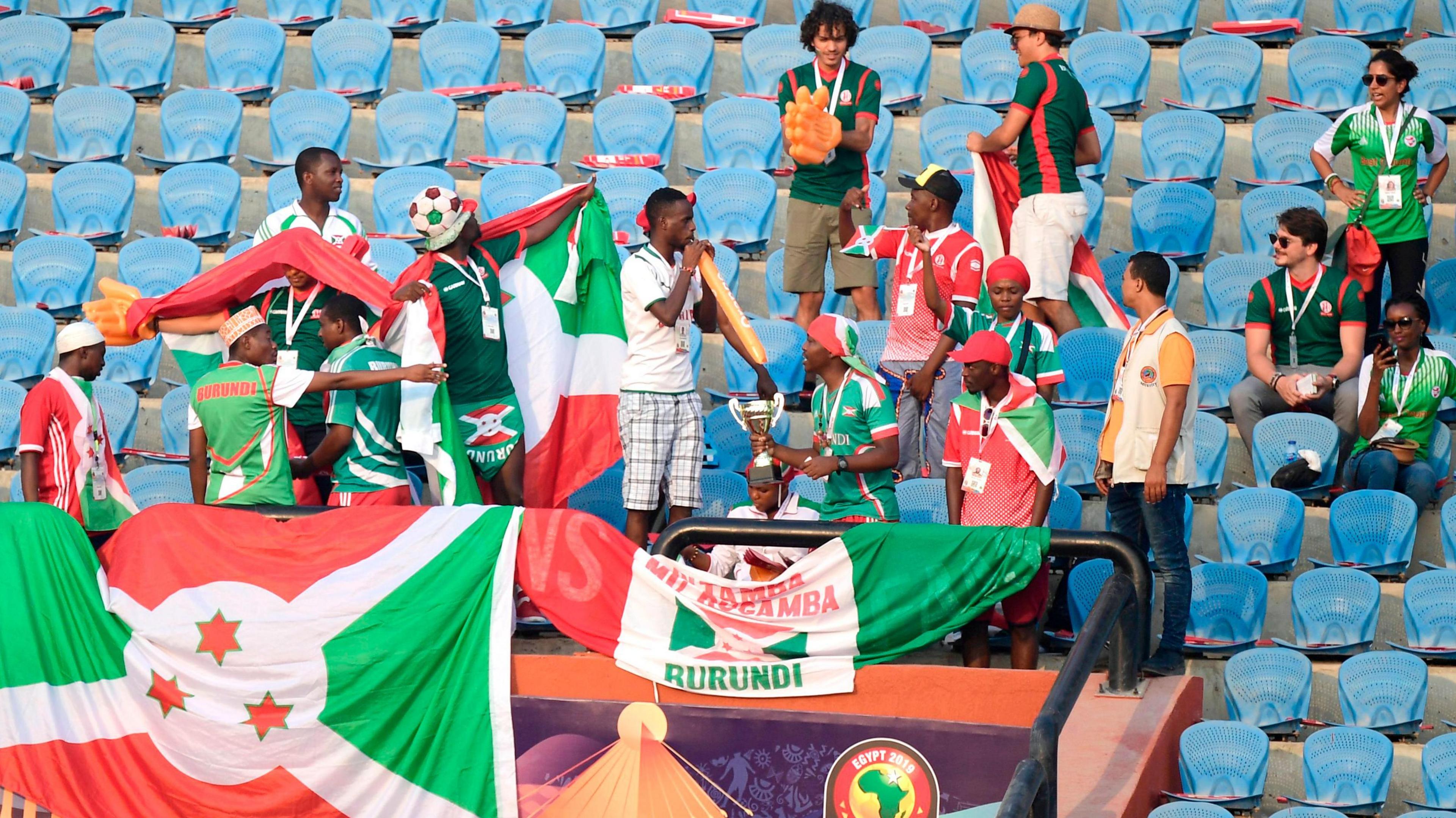 Eighteen Burundi fans standing behind the country's flag are seen spread out among rows of empty blue seats in the stands at a football game