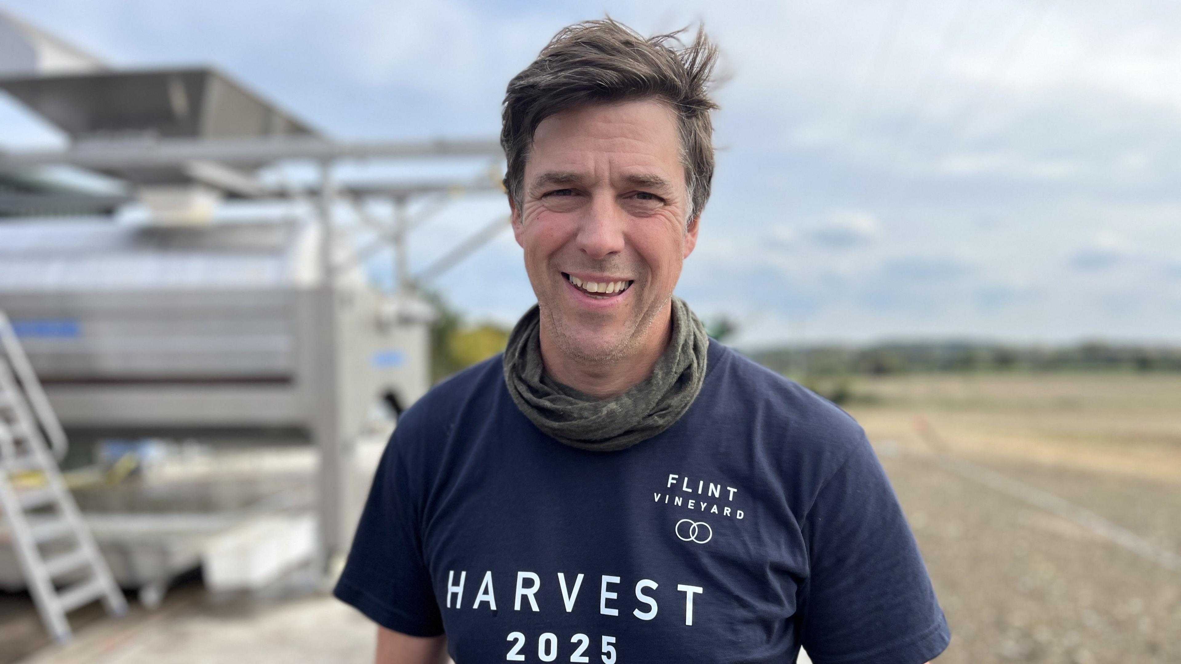 Smiling man facing camera wearing a navy blue t shirt saying Harvest 2025