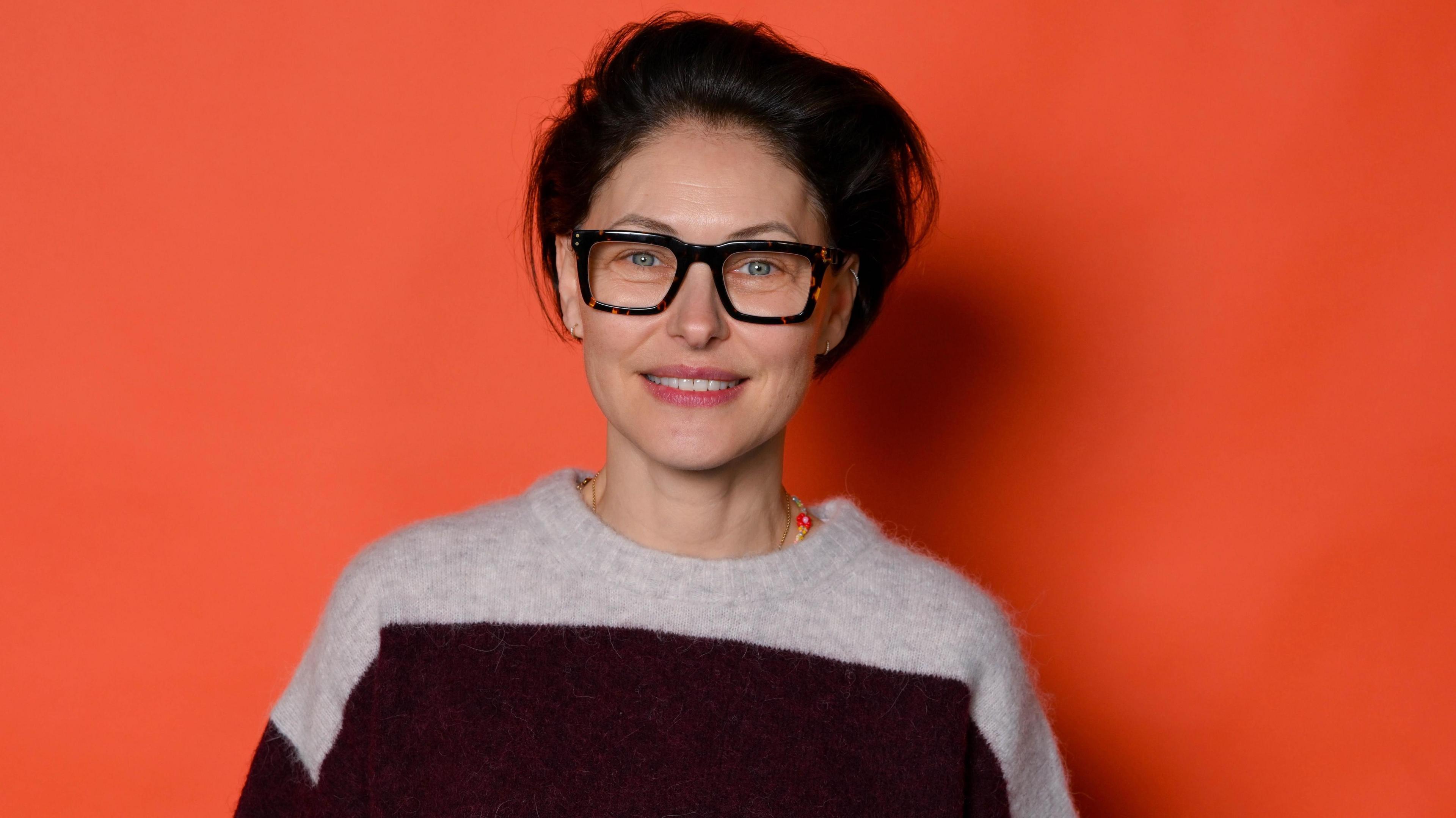 Emma WIllis wearing a stripey jumper on an orange background