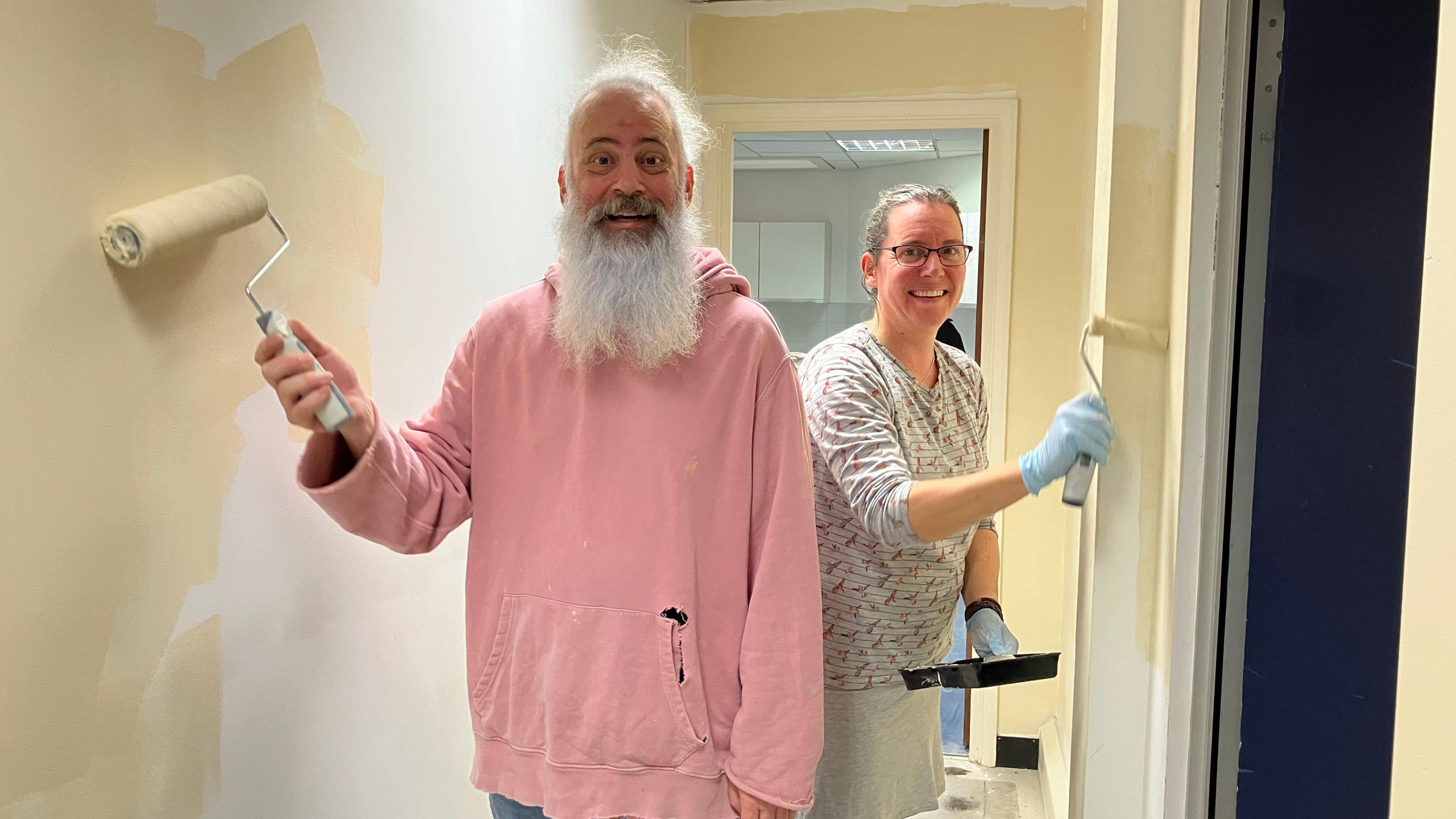Michael Andersson and Anne Plummer with paint rollers standing in a corridor with some walls white and some magnolia