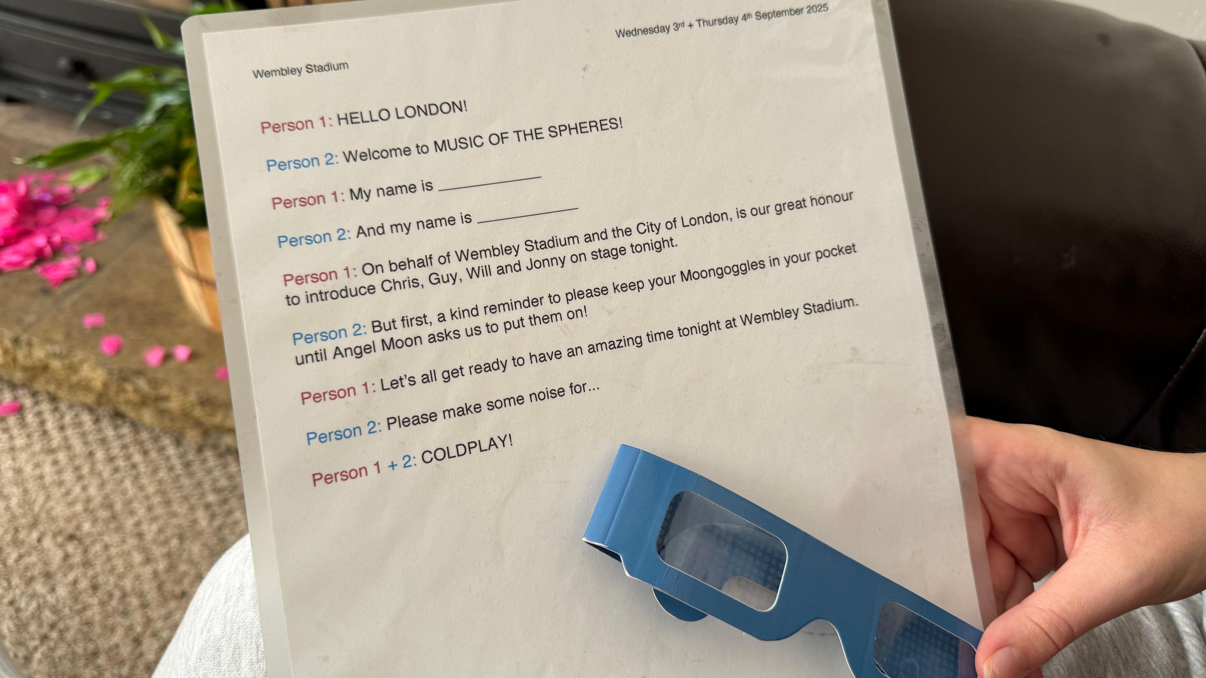 A piece of paper is being held close to the camera with a pair of 3D glasses. The paper has a script on it which reads: 
Person 1: Hello London!
Person 2: Welcome to Music of the Spheres! 
Person 1: My name is [insert name]
Person 2: And my name is [insert name]
Person 1: On behalf of Wembley Stadium and the City of London, is our great honour to introduce Chris, Guy, Will and Johnny on stage tonight.
Person 2: But first, a kind reminder to please keep your Moongoogles in your pocket until Angel Moon asks us to put them on! 
Person 1: Let's all get ready to have an amazing time tonight at Wembley Stadium.
Person 2: Please make some noise for...
Person 1 + 2: COLDPLAY!