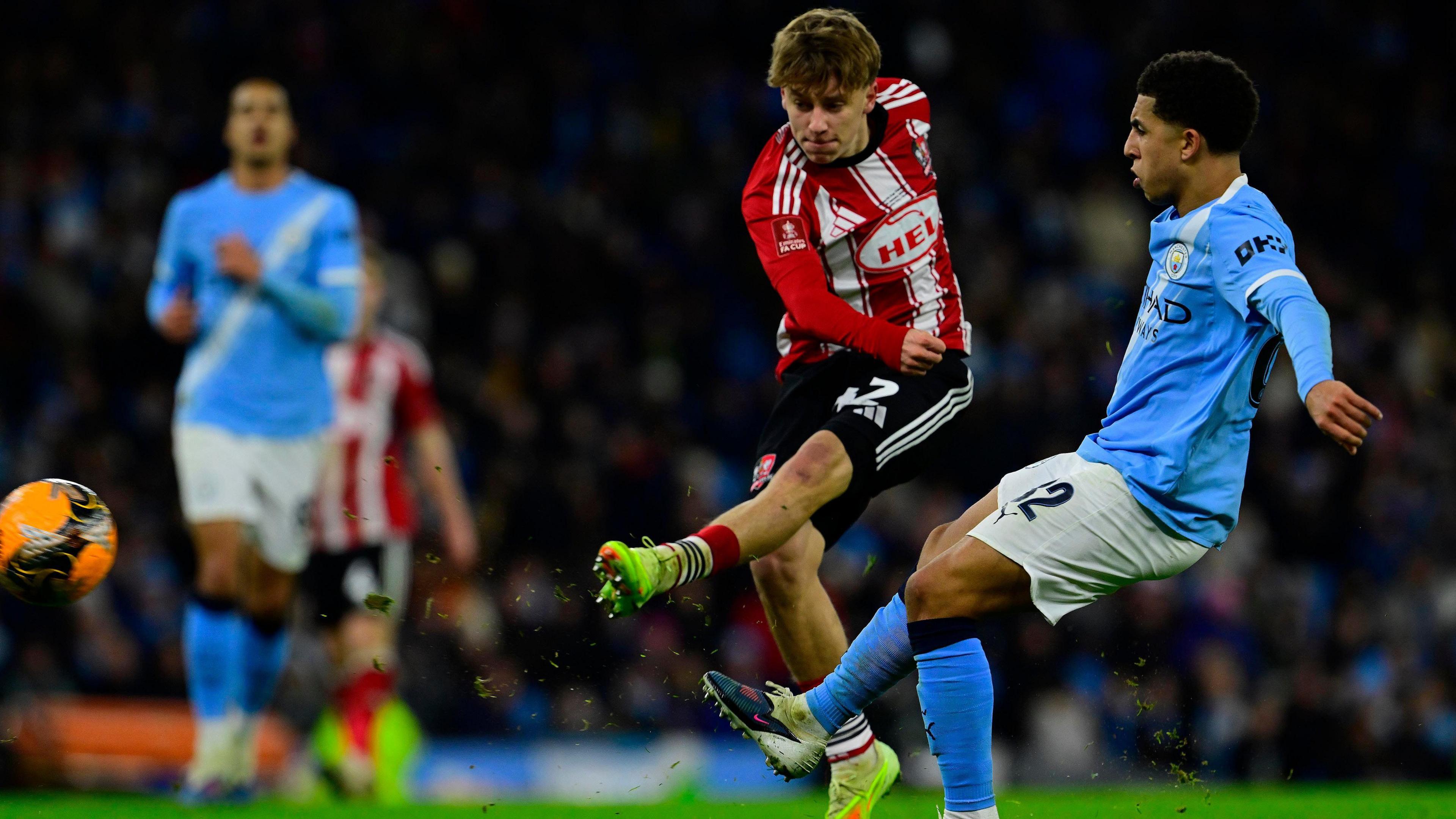 George Birch shooting with his left foot to score from outside the box against Manchester City as City defender Rico Lewis attempts to close him down.