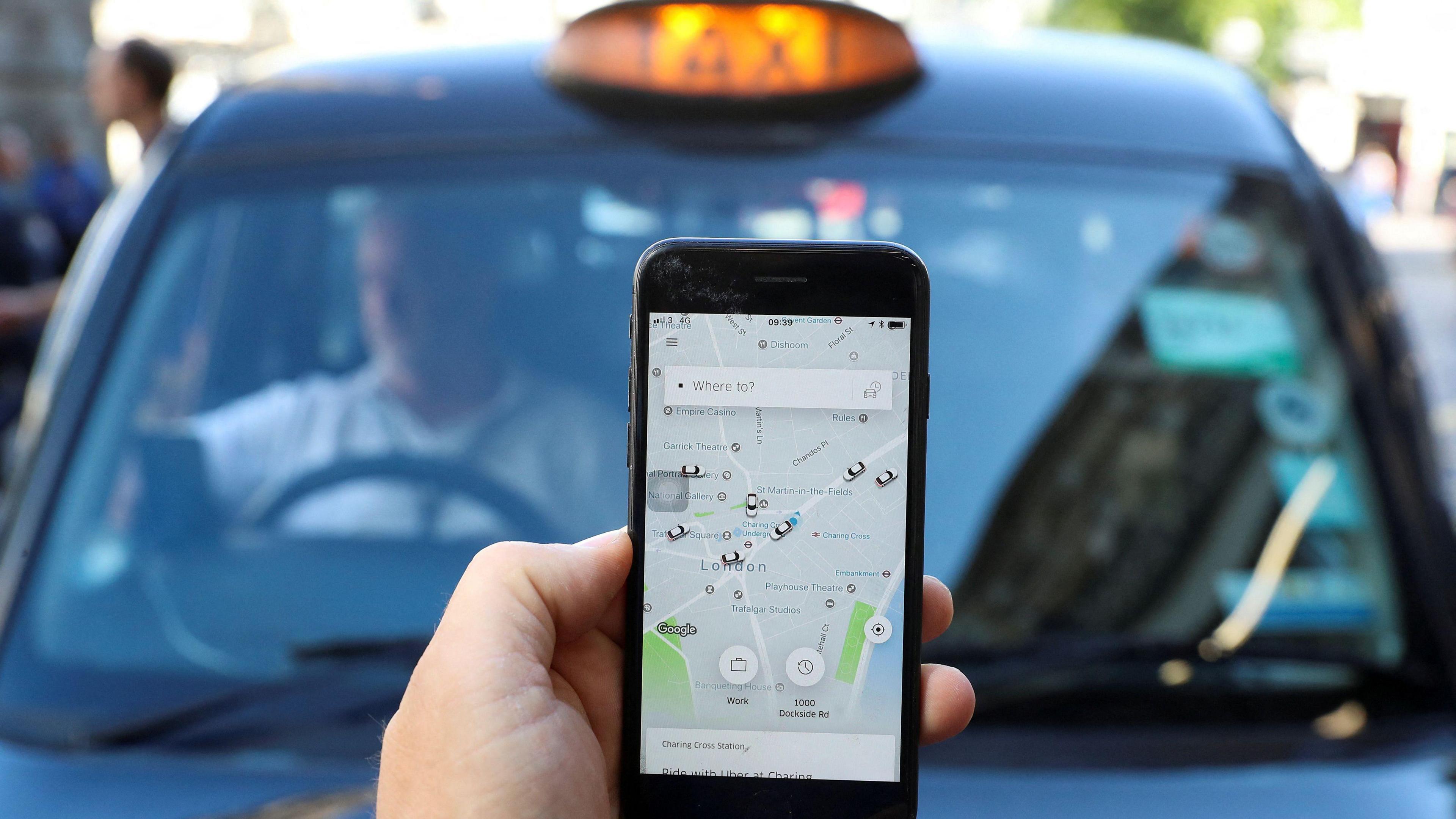 Phone showing Uber app and a London black cab in the background.