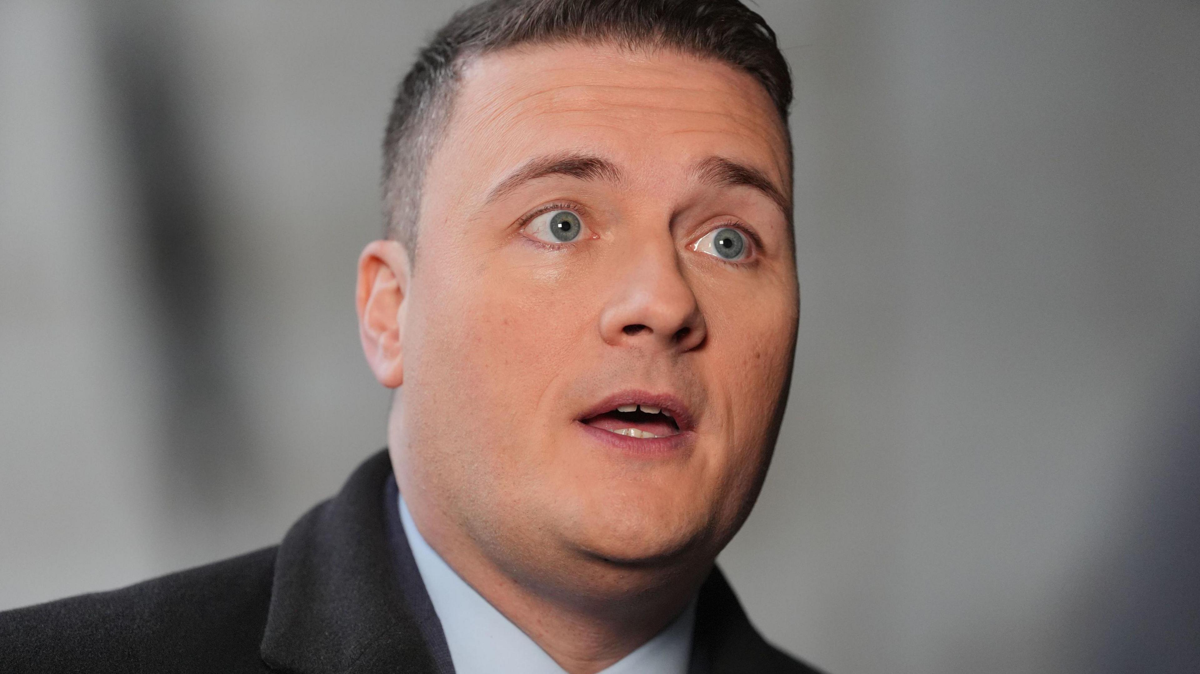 Health Secretary Wes Streeting with short brown hair and blue eyes wearing a suit and black coat.