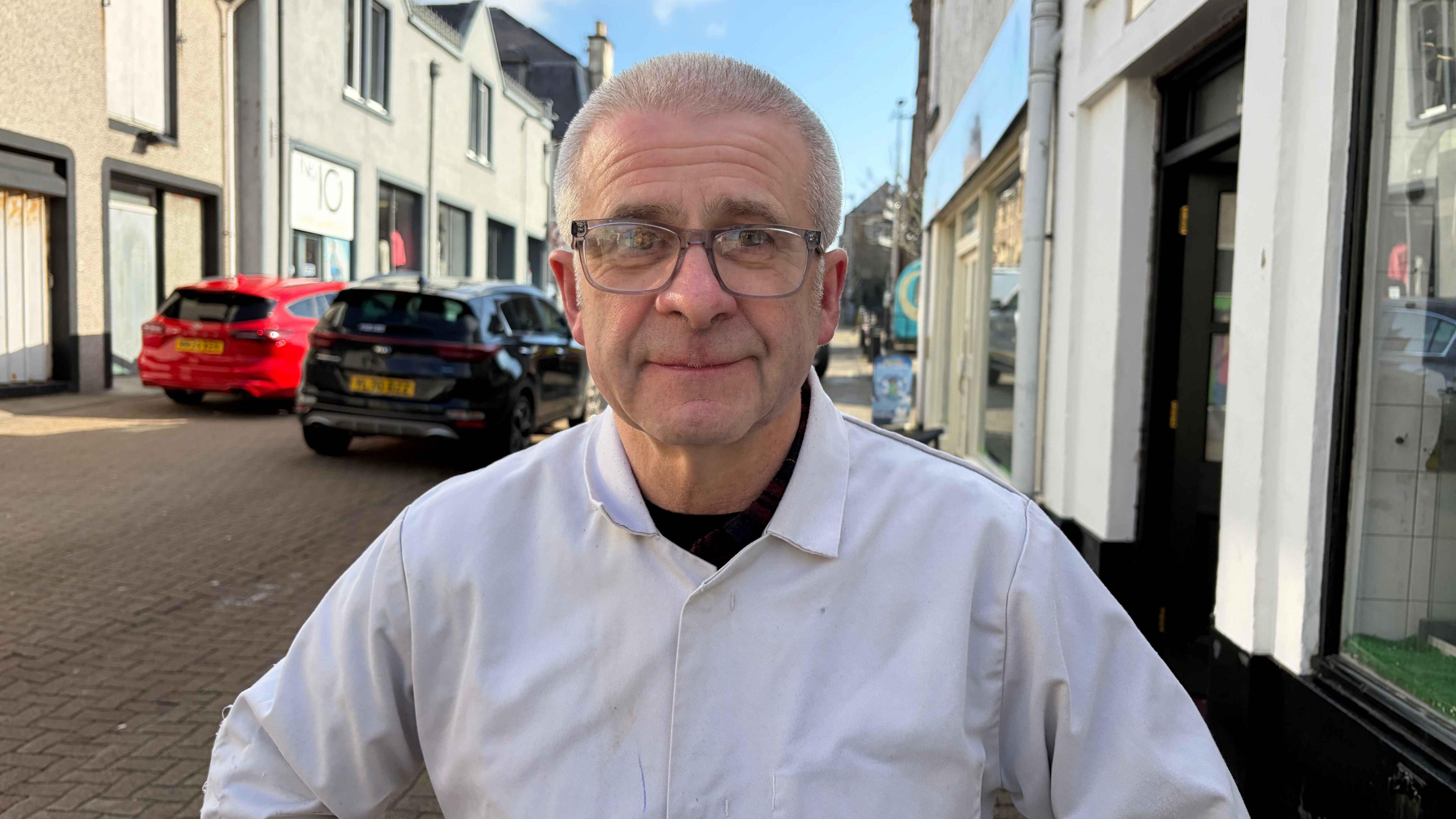 Raibeart Mac a' Ghobhainn na sheasamh taobh a-muigh bùth W.J. MacDonald