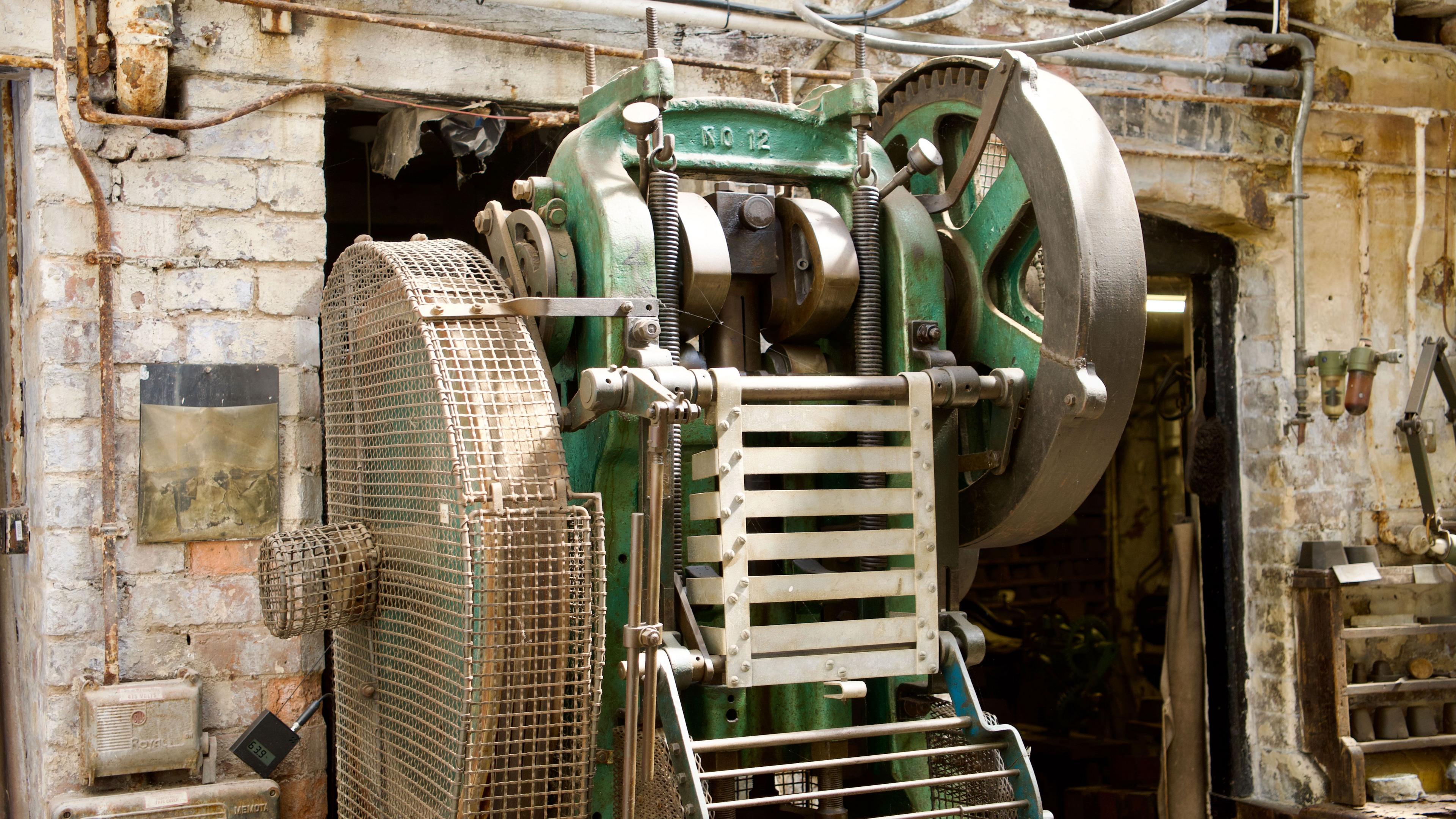 A machine with pistons and a wheel inside an old silver factory. The interior is as if the factory was still open today